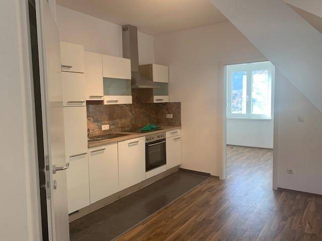 Moderne Einbauküche mit weißen Schränken, Holzboden und Dachschräge in einem hellen Raum.