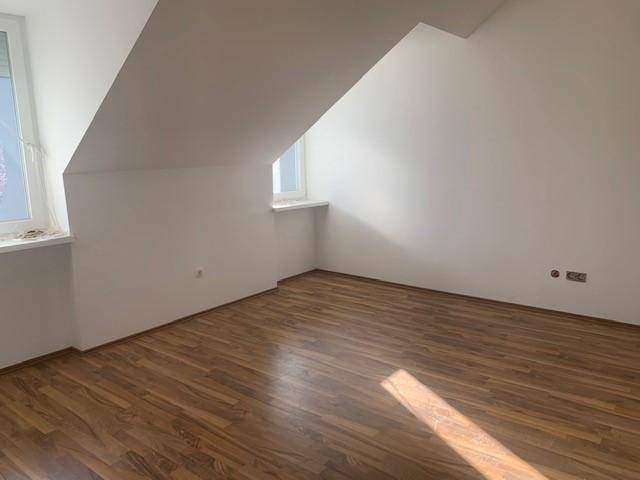 Geräumiges Zimmer im Dachgeschoss mit Laminatboden, Dachschräge und viel natürlichem Licht.