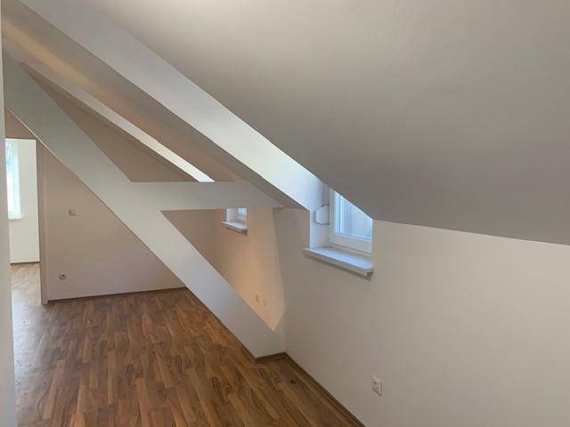 Heller Wohnbereich im Dachgeschoss mit Holzboden, sichtbaren Dachbalken und Fenstern.