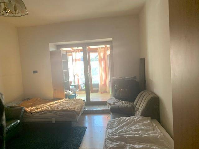 Wohnzimmer mit Betten und einem Sofa, das zu einem verglasten Balkon oder Wintergarten führt.
