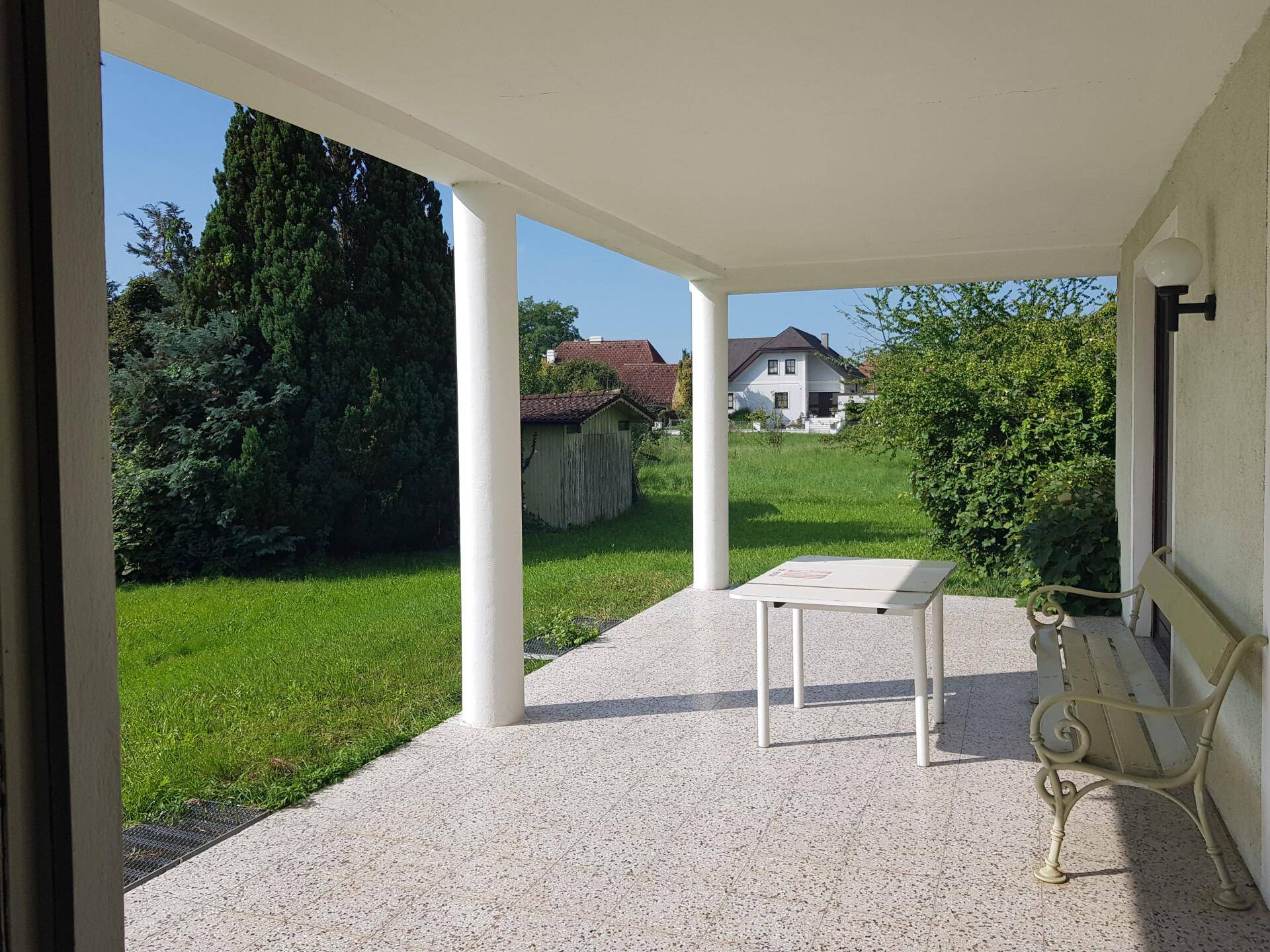 Überdachte Terrasse mit Sitzgelegenheiten und Blick auf den Garten und die Nachbarschaft.