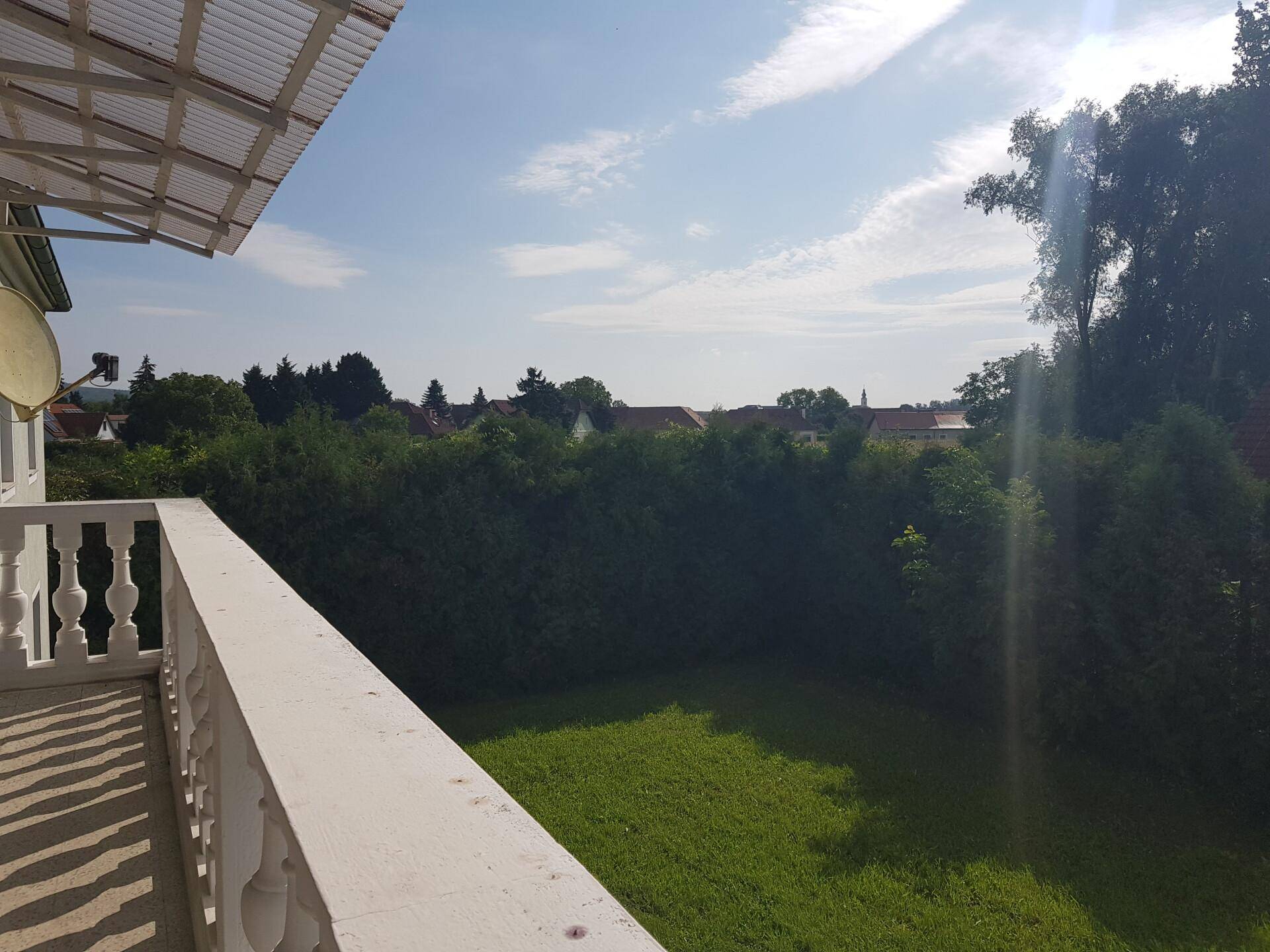 Panoramablick vom Balkon über die grüne Landschaft und die Dächer der umliegenden Häuser.