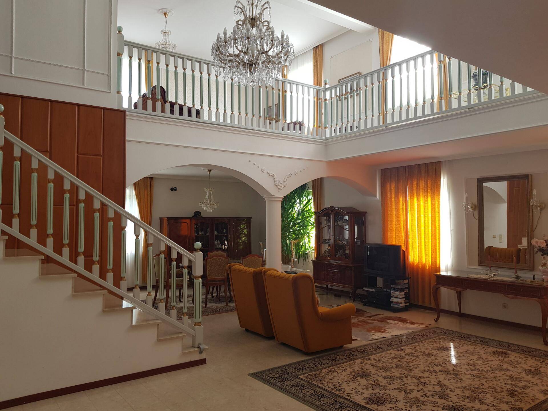 Repräsentativer Wohnbereich mit hoher Decke, Kronleuchter, Treppe und Galerie, klassisch eingerichtet.