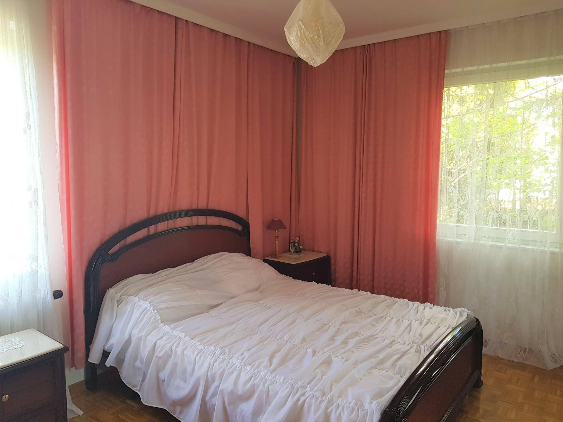Gemütliches Schlafzimmer mit Doppelbett, Holzparkett und rosa Vorhängen, hell und einladend.