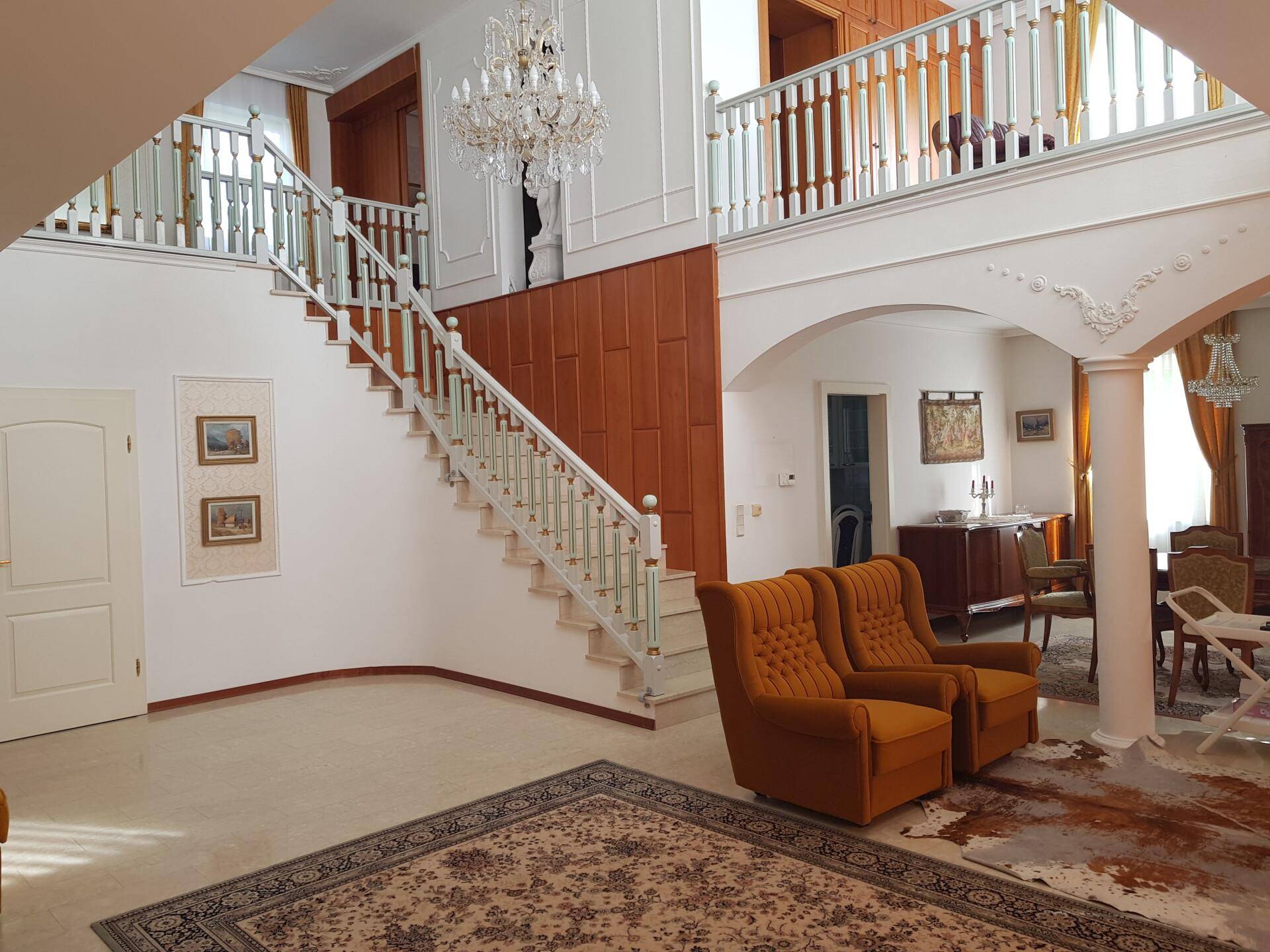 Heller Wohnbereich mit eleganter Treppe, hohen Decken und klassischem Mobiliar, das zum Verweilen einlädt.