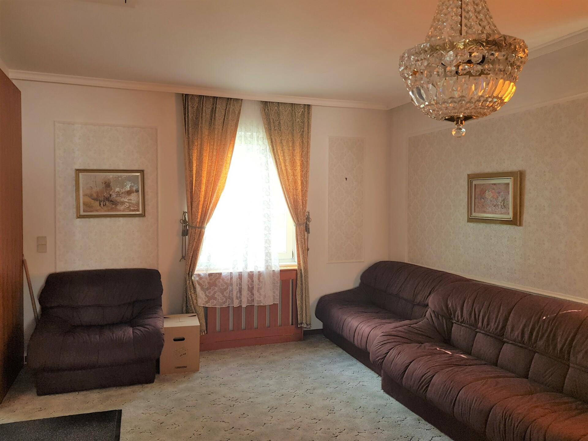 Helles Wohnzimmer mit großen Fenstern, Fliesenboden und klassischer Einrichtung, einladend gestaltet.