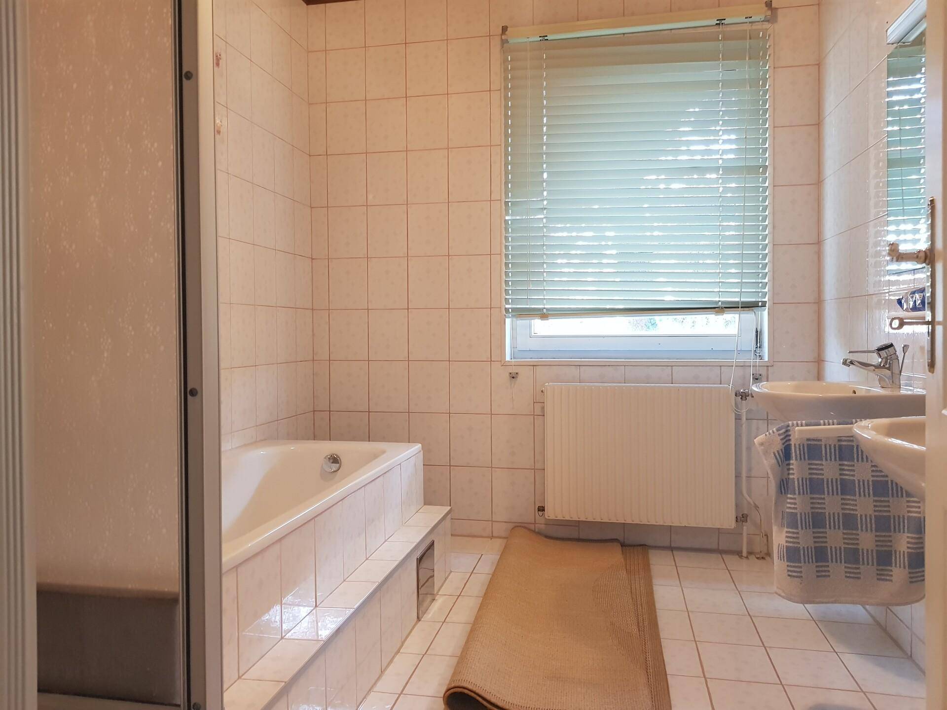 Gefliestes Badezimmer mit Badewanne, Dusche und Fenster, in einem hellen, funktionalen Design.
