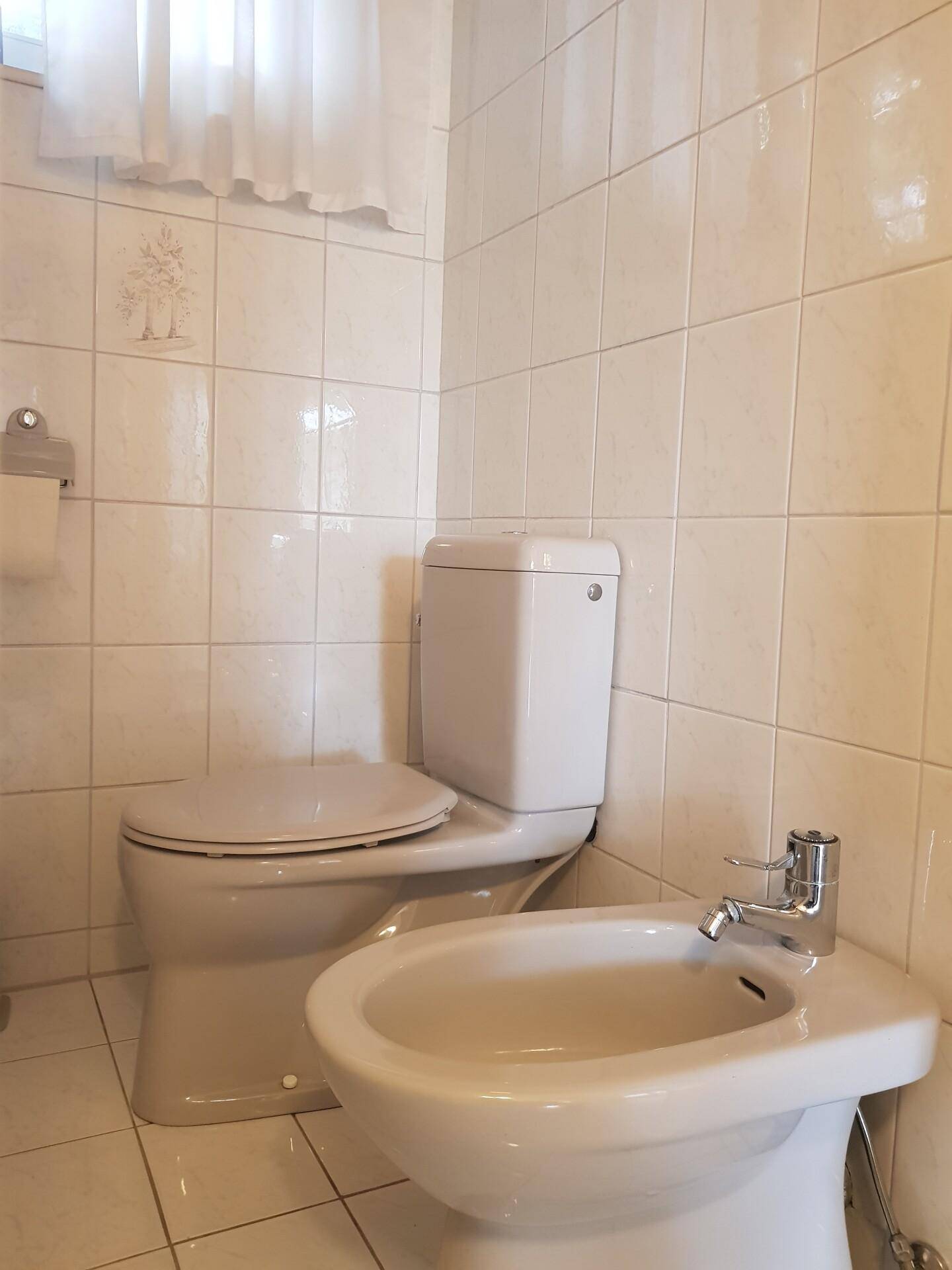 Separate Toilette mit Bidet und Fenster, komplett gefliest in hellem Farbton.