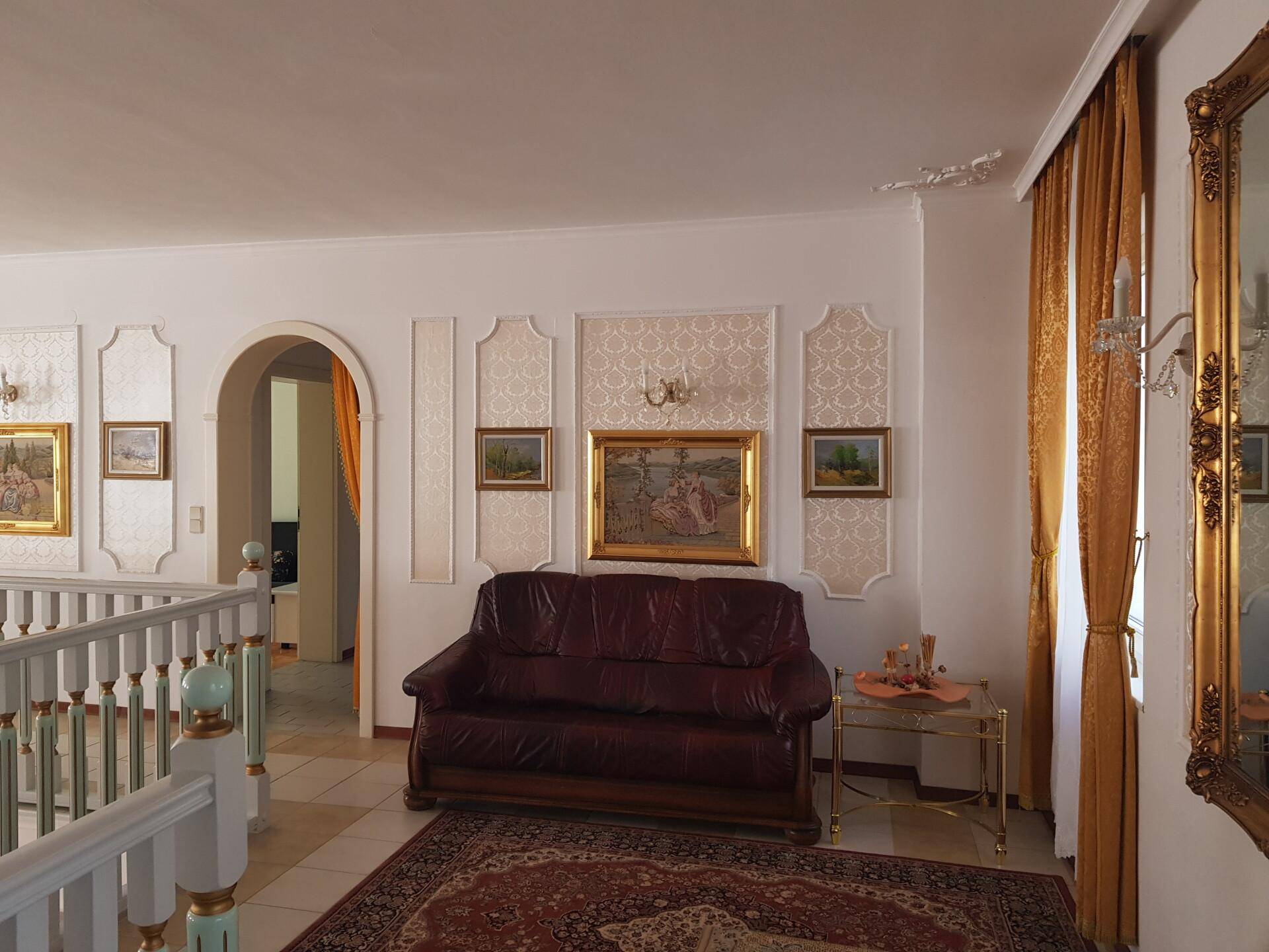Weitläufiger Blick von der Galerie auf den hellen Wohnbereich mit großen Fenstern und Kronleuchter.