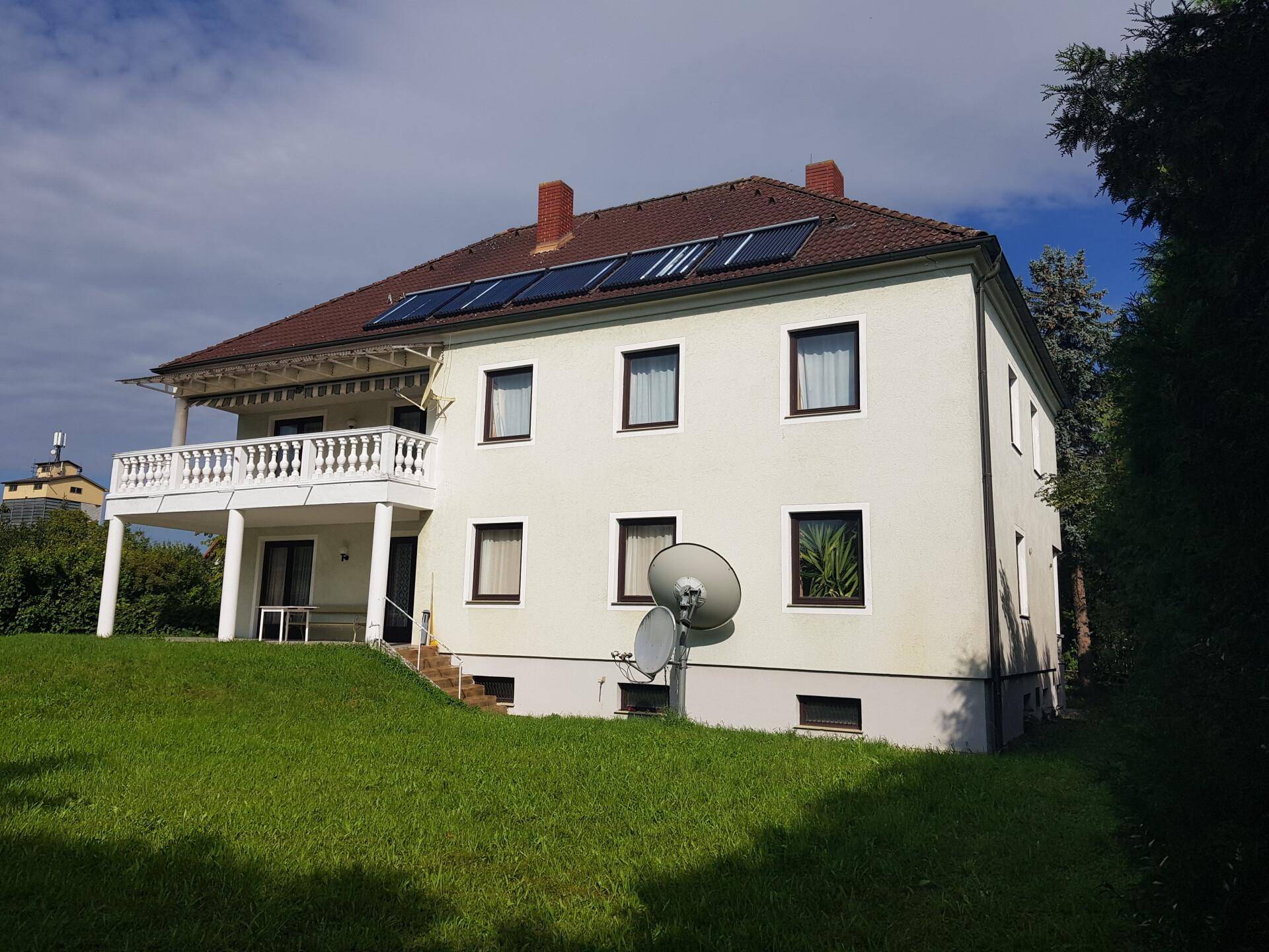 Ansicht des Wohnhauses von der Seite mit Balkon, überdachter Terrasse und gepflegtem Garten.