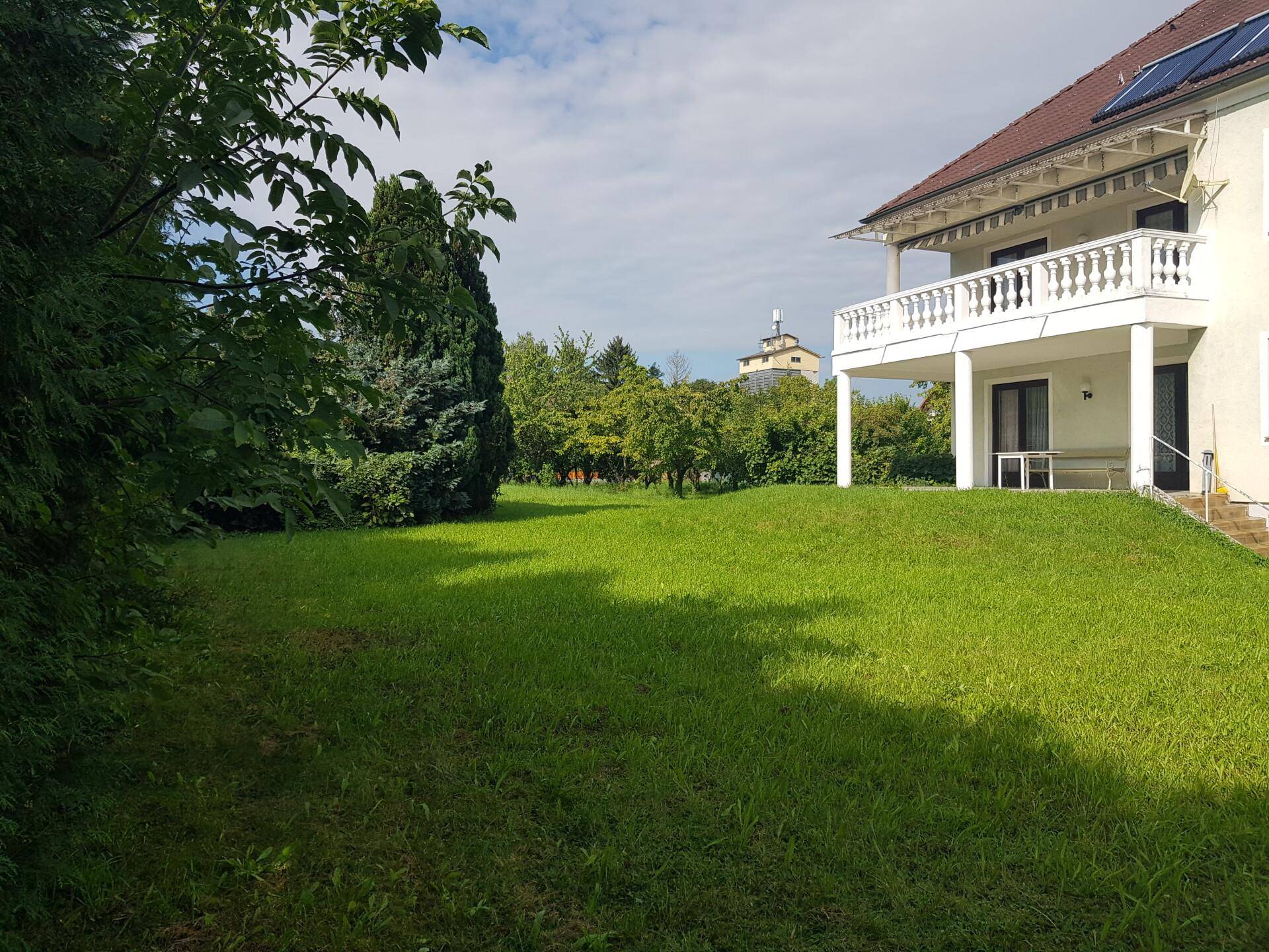 Vorderansicht des Wohnhauses mit Eingangsbereich, Treppe und Balkon, umgeben von Bäumen.