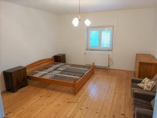 Schlafzimmer mit Holzbett, Nachttischen und Dielenboden, hell durch großes Fenster.