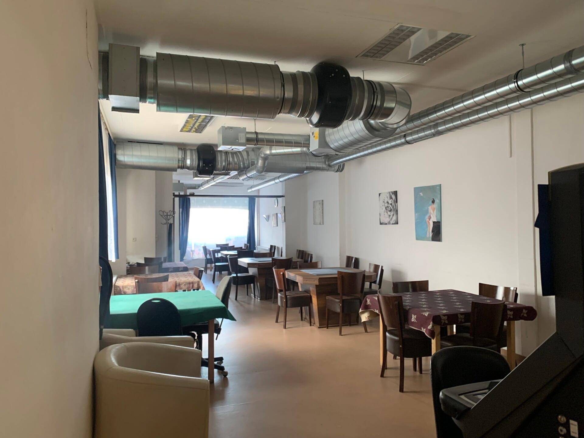 Großer Gastraum mit Tischen und Stühlen, charakterisiert durch sichtbare Lüftungsrohre an der Decke.
