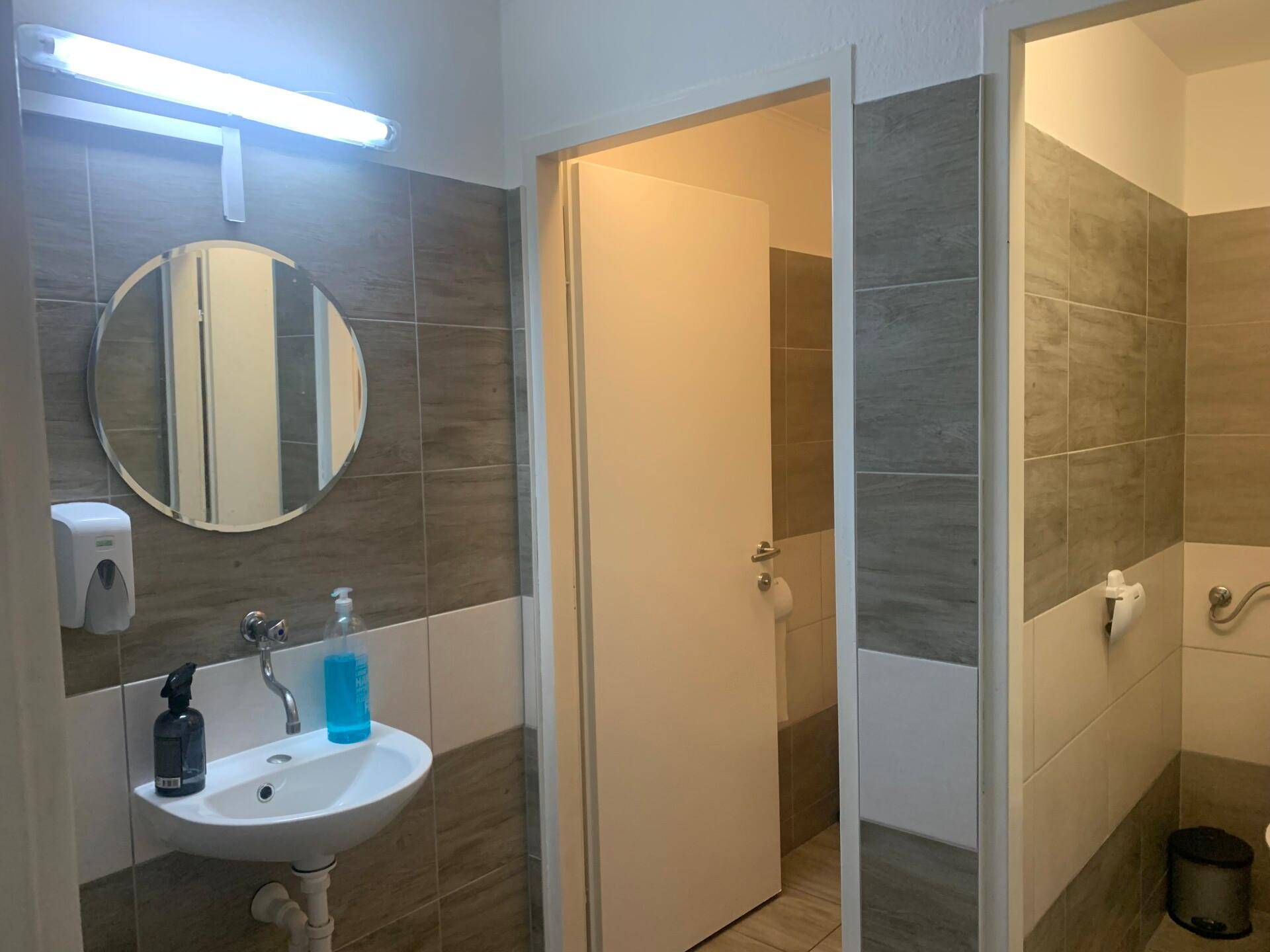 Modern gefliestes Badezimmer mit Waschbecken, rundem Spiegel und zweifarbigen Wandfliesen.