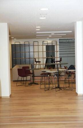 Geräumiger Flur mit Holzboden und einem Regal als Raumteiler, der zu einem offenen Bürobereich führt.