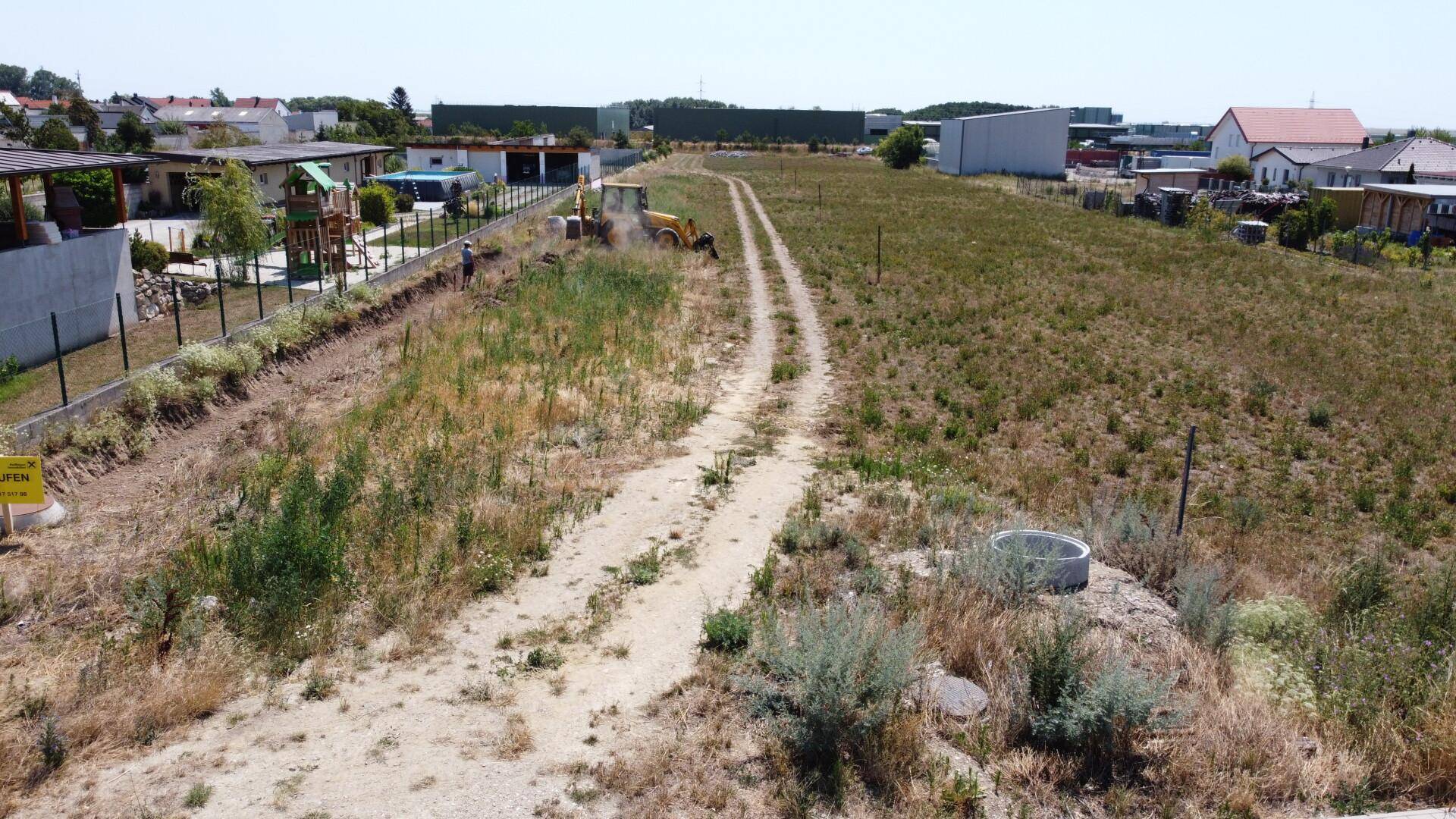Weitläufiges Grundstück mit einem Feldweg, Baumaschinen und angrenzenden Wohnhäusern.