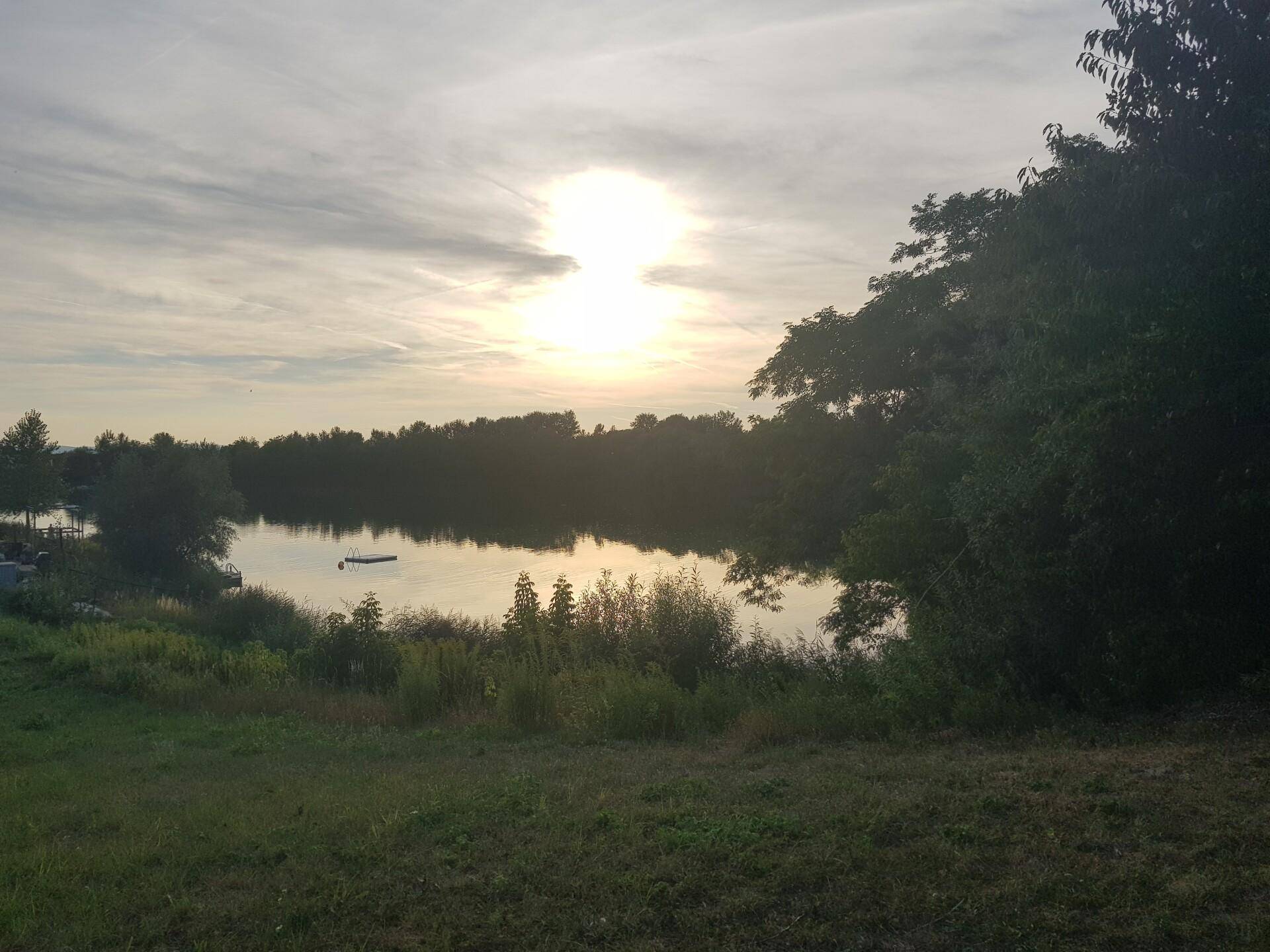 Malerischer Blick auf einen ruhigen See bei Sonnenuntergang, umgeben von üppiger Natur.