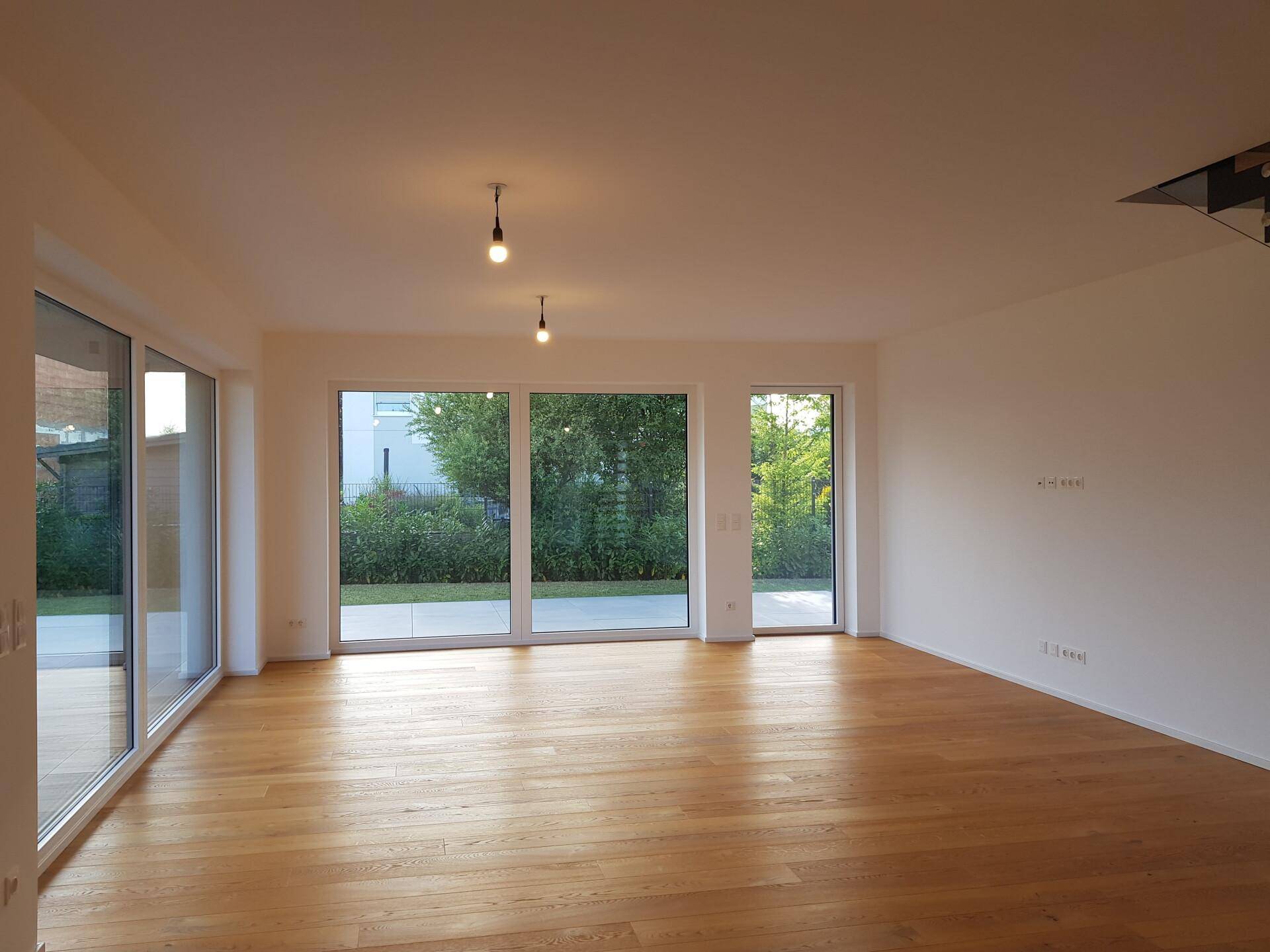 Heller, leerer Wohnraum mit Eichenparkett und großen Fensterfronten zum Garten.