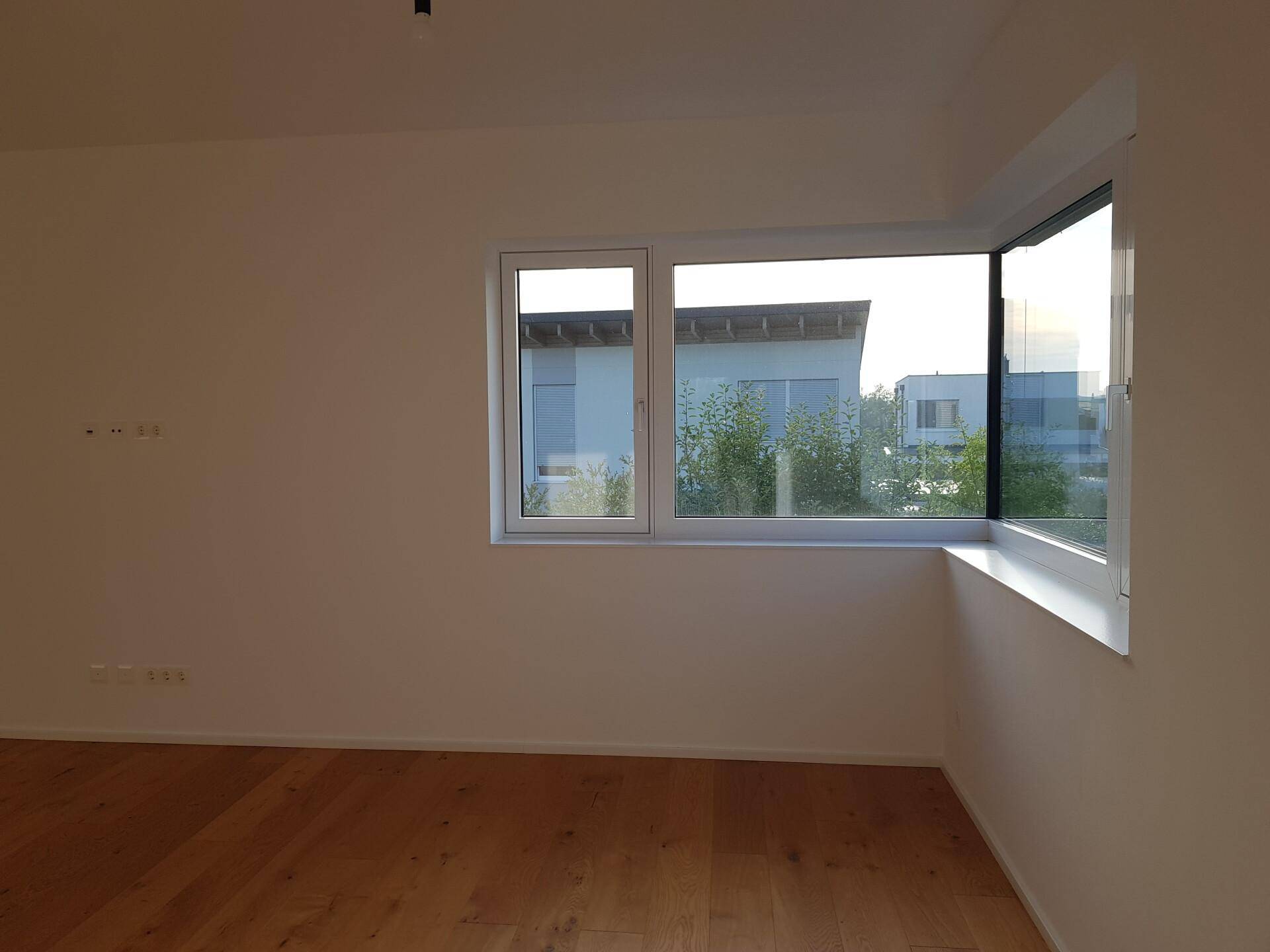Lichtdurchflutetes Zimmer mit großen Eckfenstern und Blick auf die Nachbarschaft.