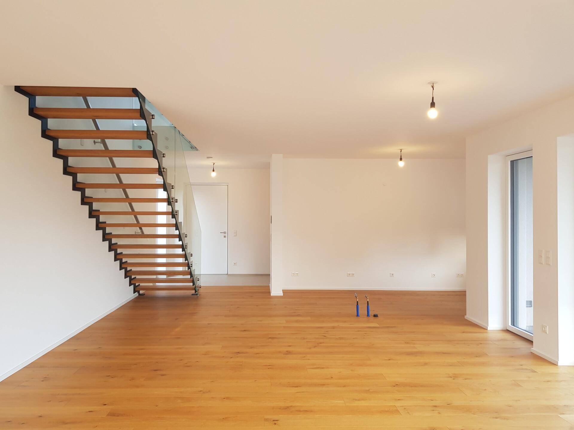 Geräumiger Wohnbereich mit moderner Holztreppe und Glasgeländer, bereit zur individuellen Gestaltung.