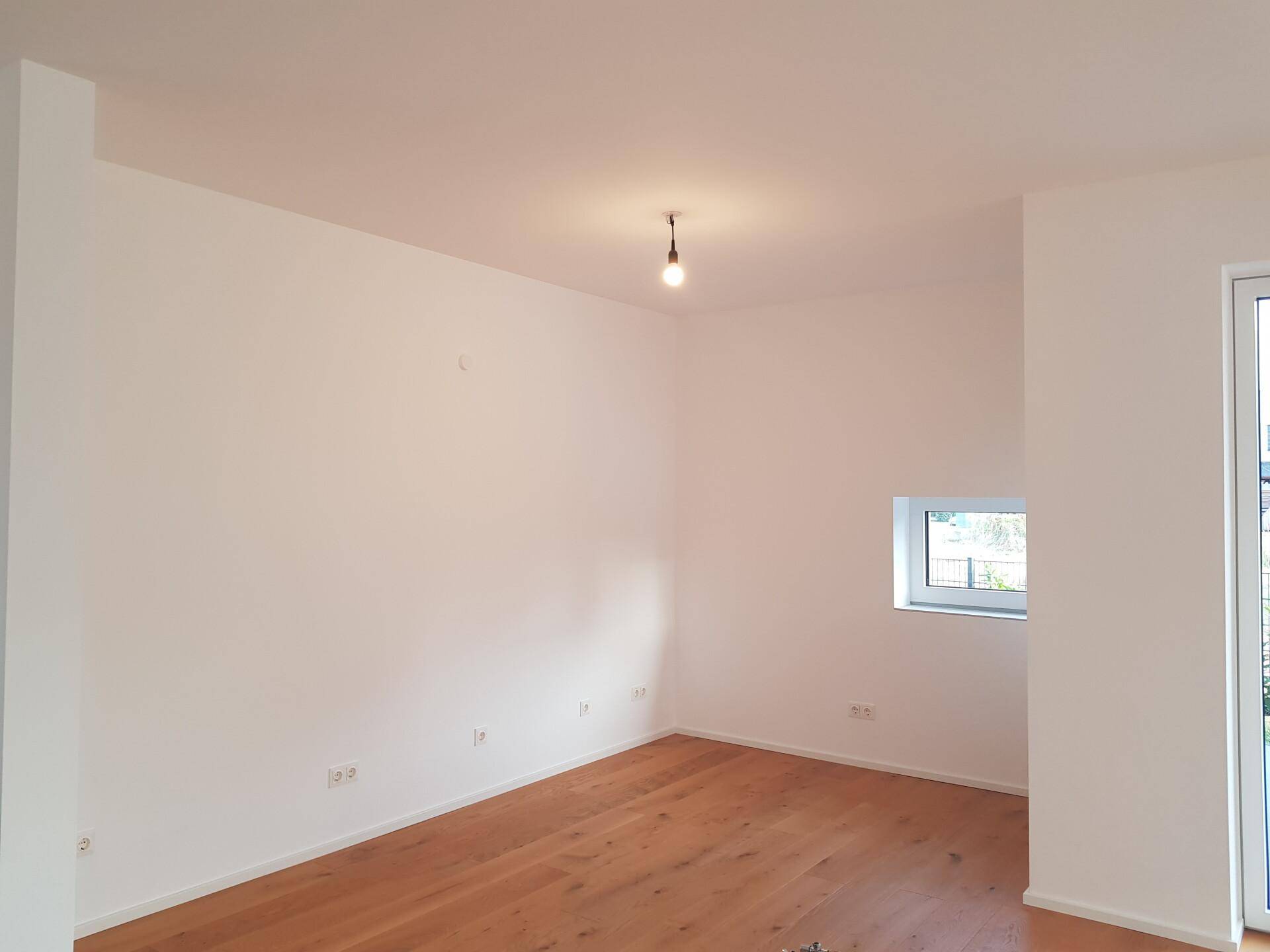 Helles Zimmer mit Parkettboden und einem Fenster, das viel Tageslicht hereinlässt.