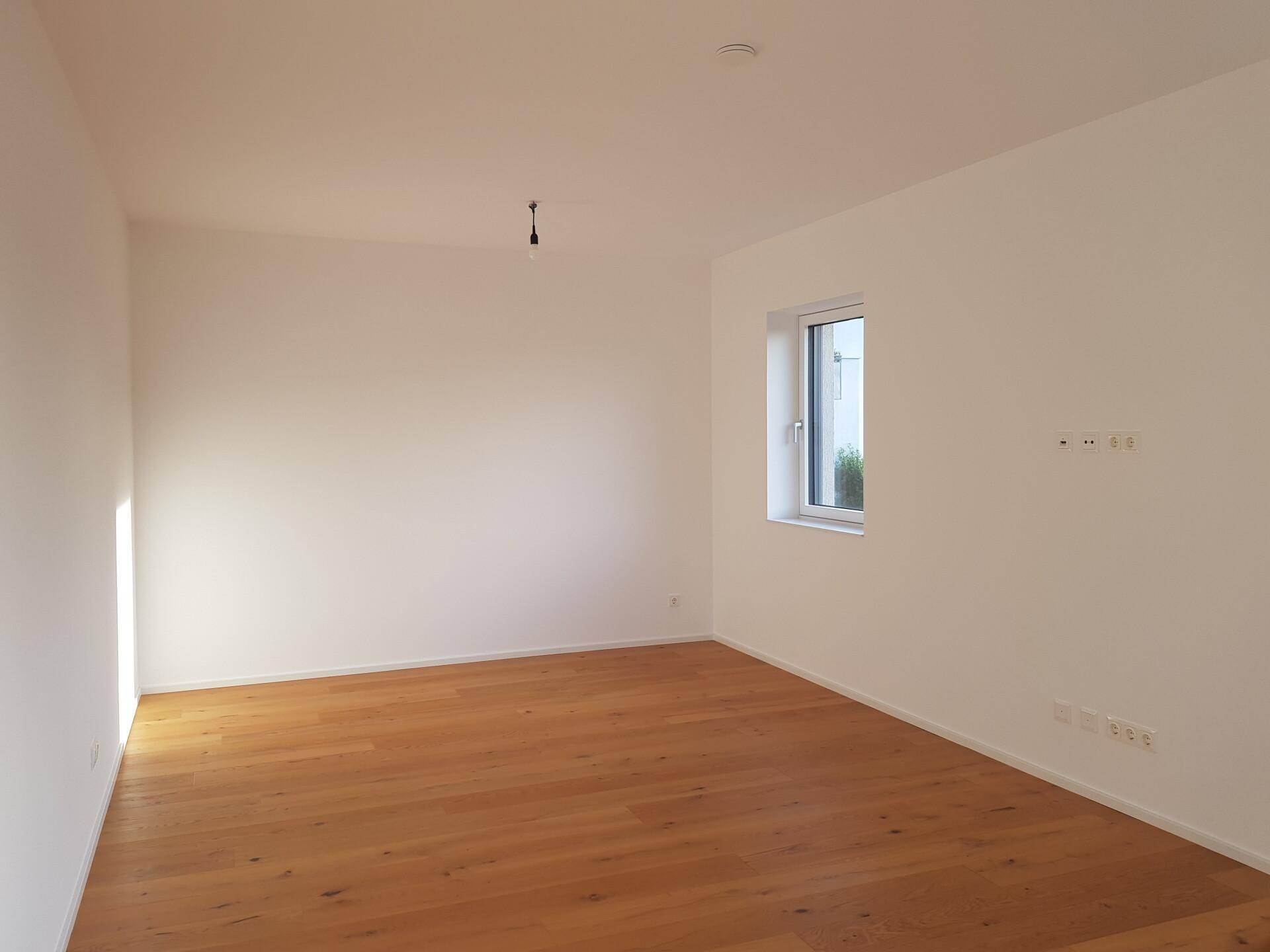 Geräumiges Schlafzimmer mit hellem Parkettboden und einem großen Fenster für viel Tageslicht.