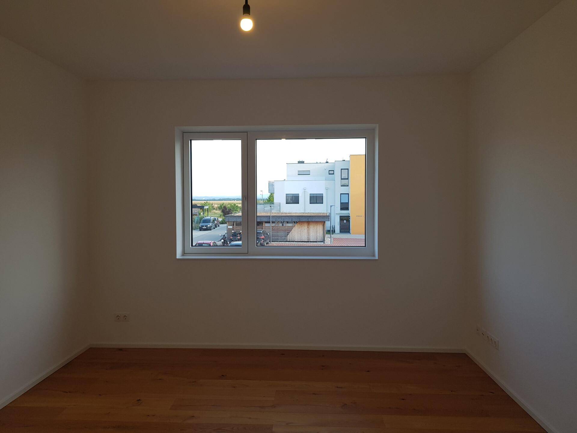Helles Zimmer mit Parkettboden und einem Fenster, das einen Blick auf die Umgebung ermöglicht.