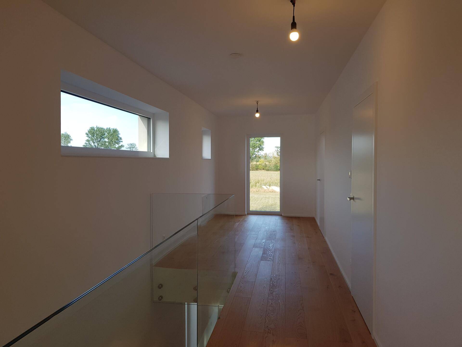 Heller Flur im Obergeschoss mit Parkettboden, Fenster und Zugang zu weiteren Räumen.