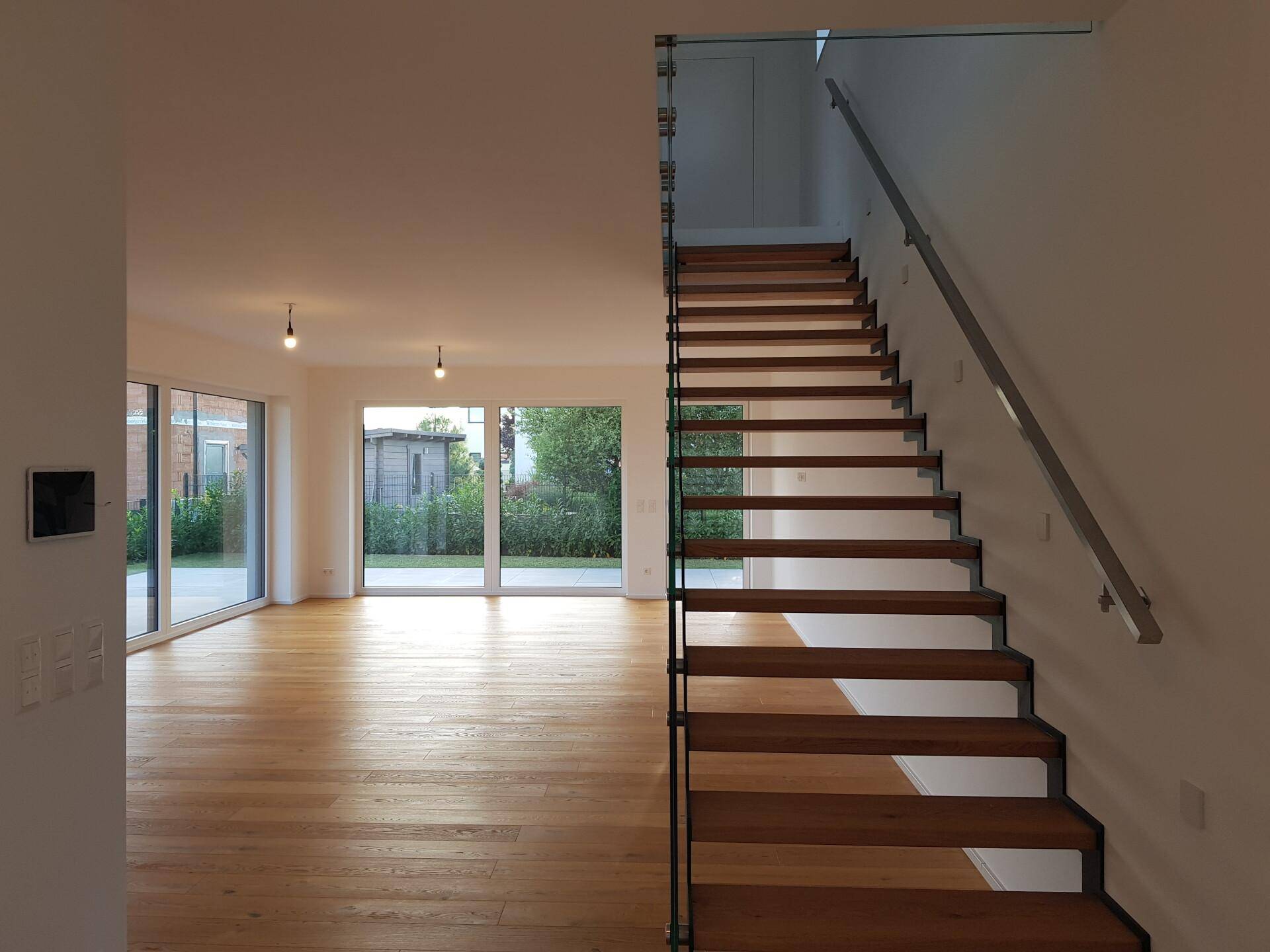Offener Wohnbereich mit eleganter Holztreppe, Glasgeländer und Blick in den Garten.