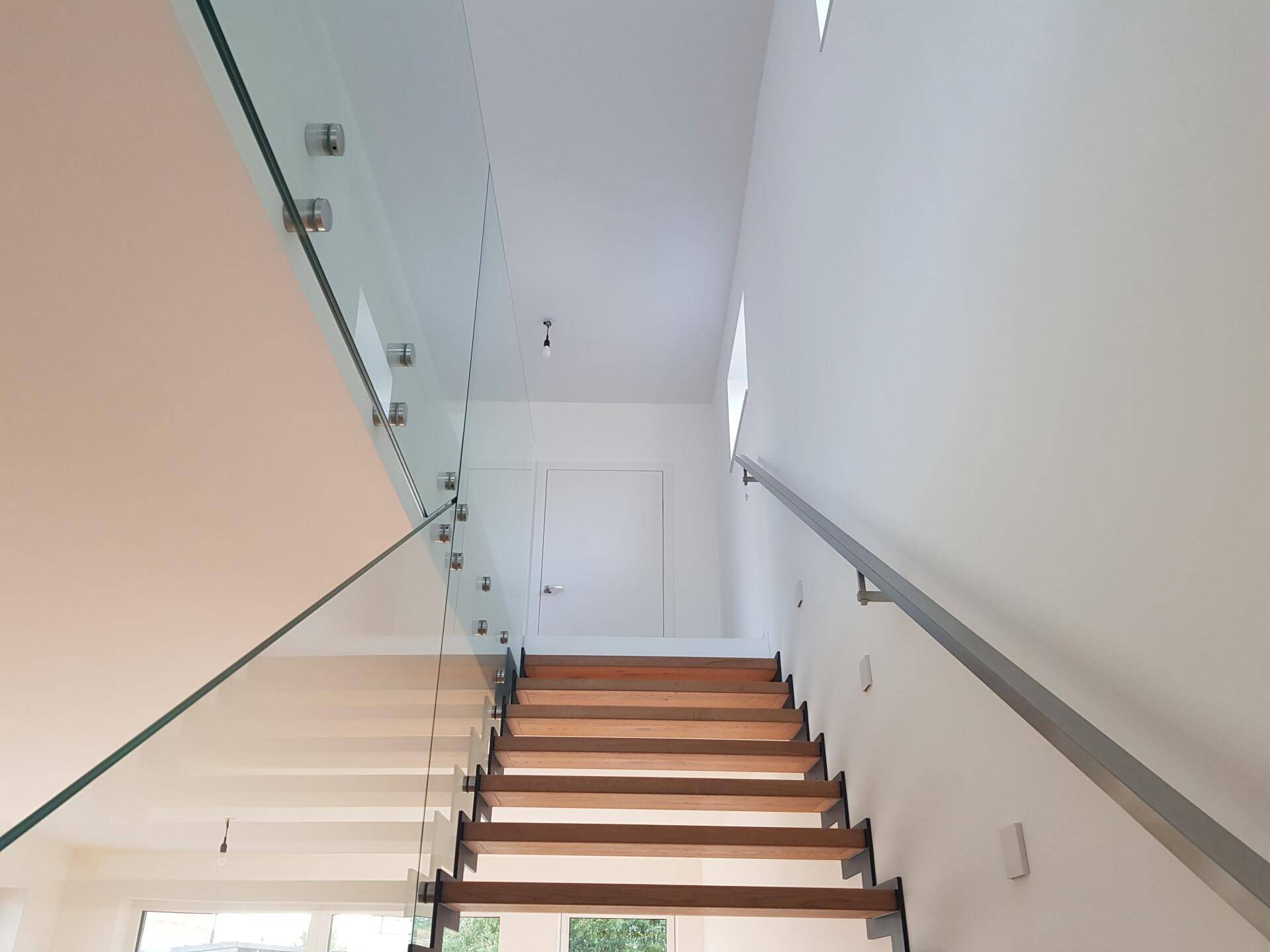 Moderne Treppe mit Holzstufen und Glasgeländer, die die oberen Etagen erschließt.