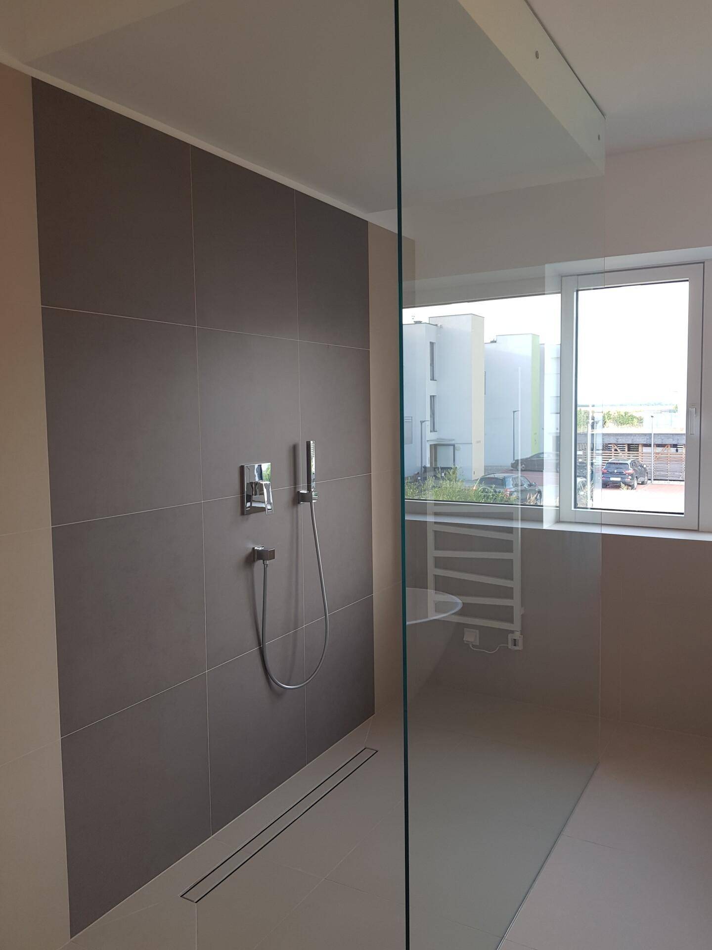 Ebenerdige Dusche mit Glasabtrennung und modernen Armaturen in einem hellen Badezimmer.