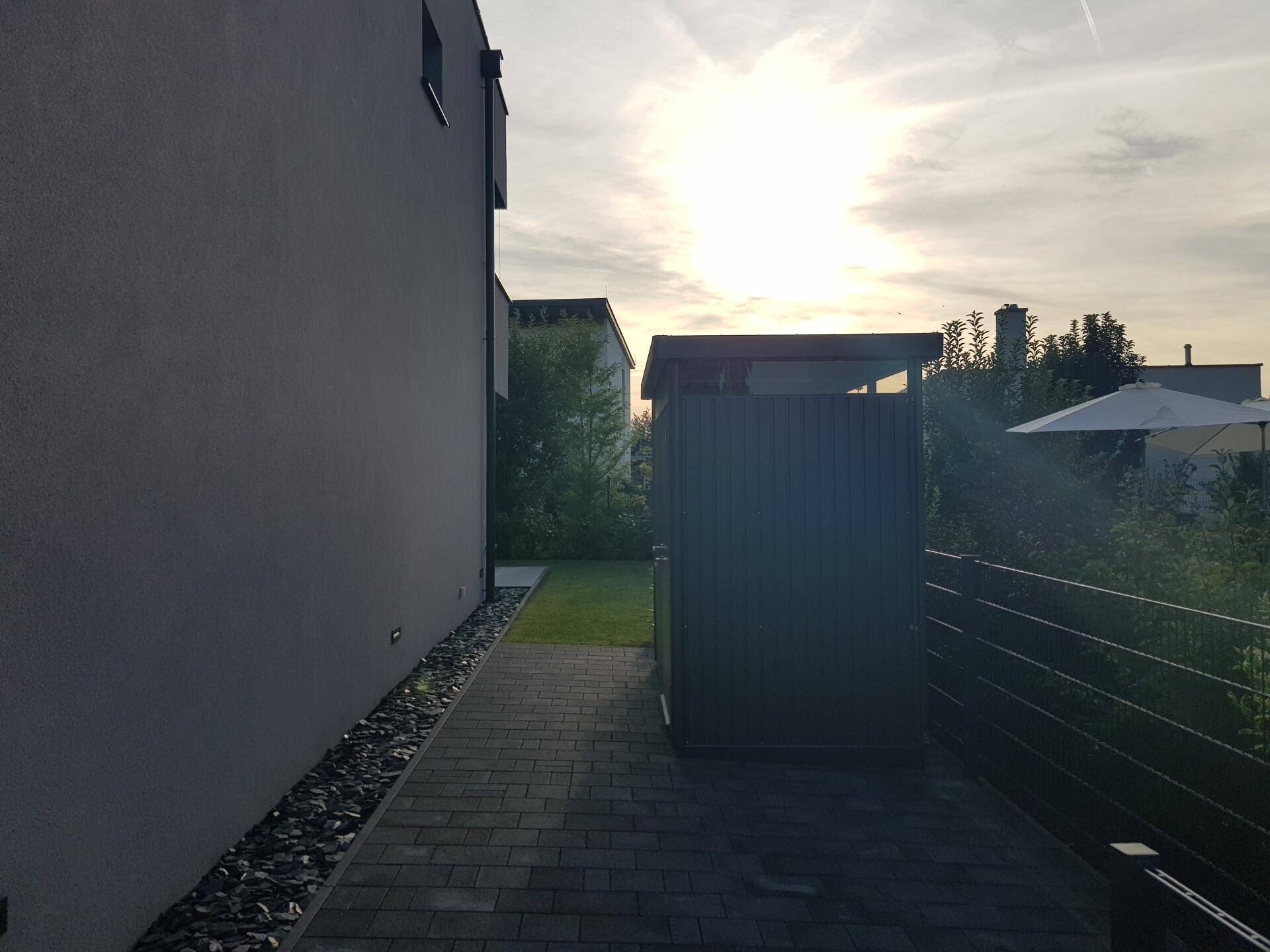Seitlicher Zugang zum Haus mit gepflastertem Weg und einem kleinen Gartenschuppen.
