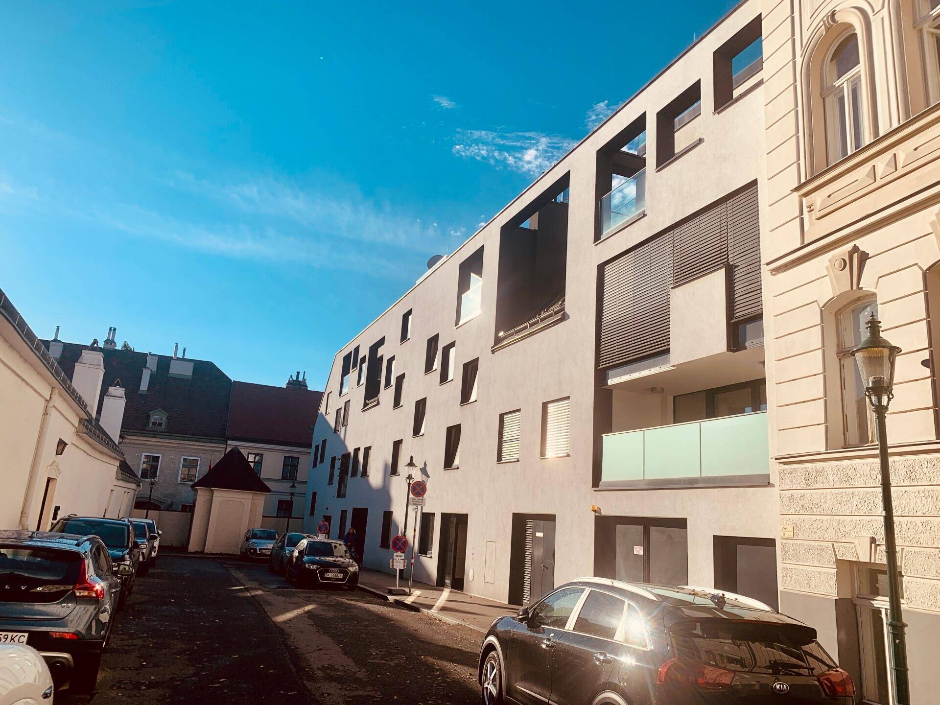 Moderne Gebäudefassade mit großen Fenstern und einem geparkten Auto auf der Straße unter blauem Himmel.