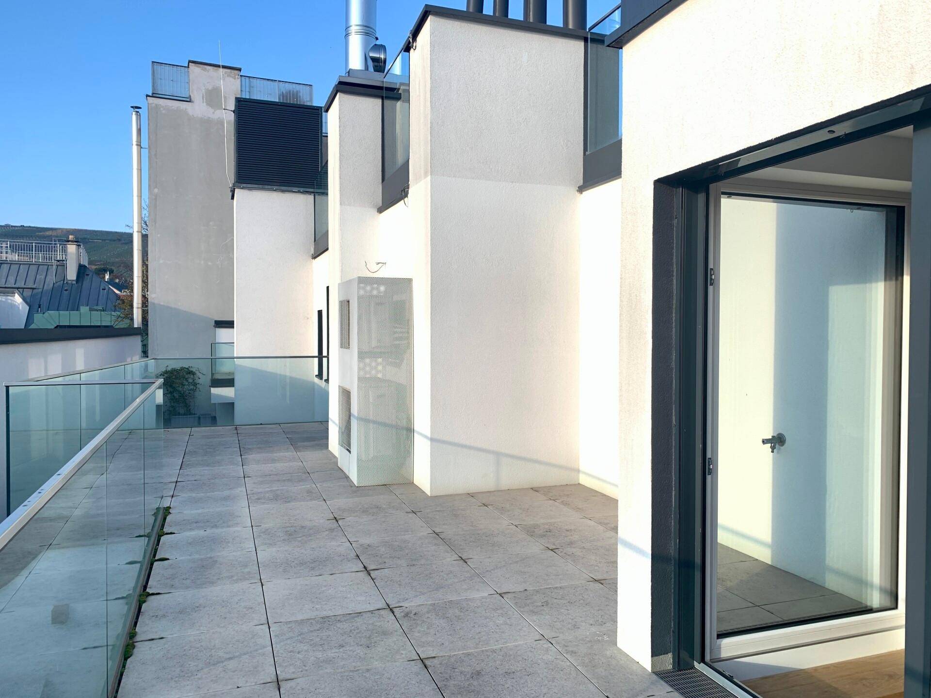 Geräumige Terrasse mit Fliesenboden und Zugang zu einem hellen Innenraum.