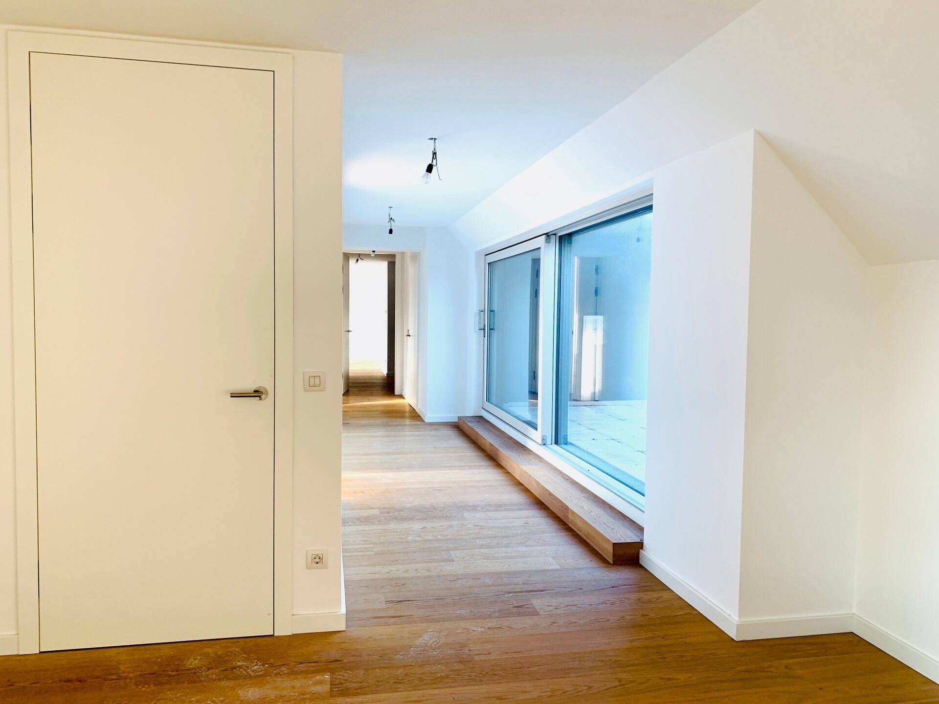 Heller Flur mit Holzboden und einer modernen Tür, die zu weiteren Räumen führt.