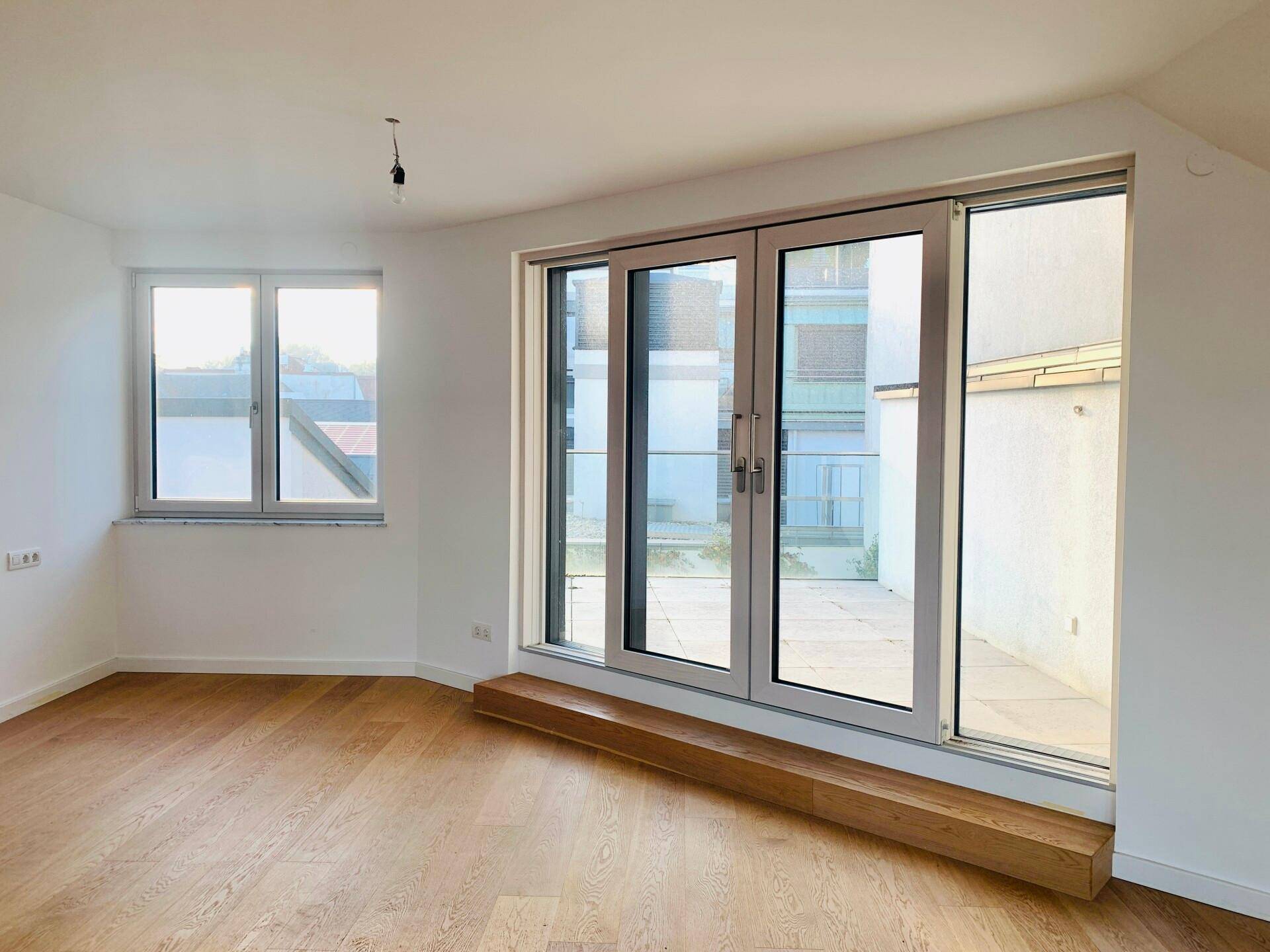 Lichtdurchfluteter Raum mit Holzboden und Zugang zu einem Außenbereich durch große Türen.