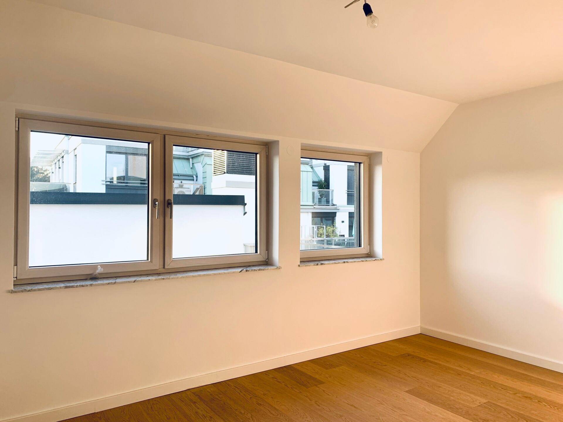 Heller Raum mit Holzboden und zwei Fenstern, die viel Tageslicht hereinlassen.