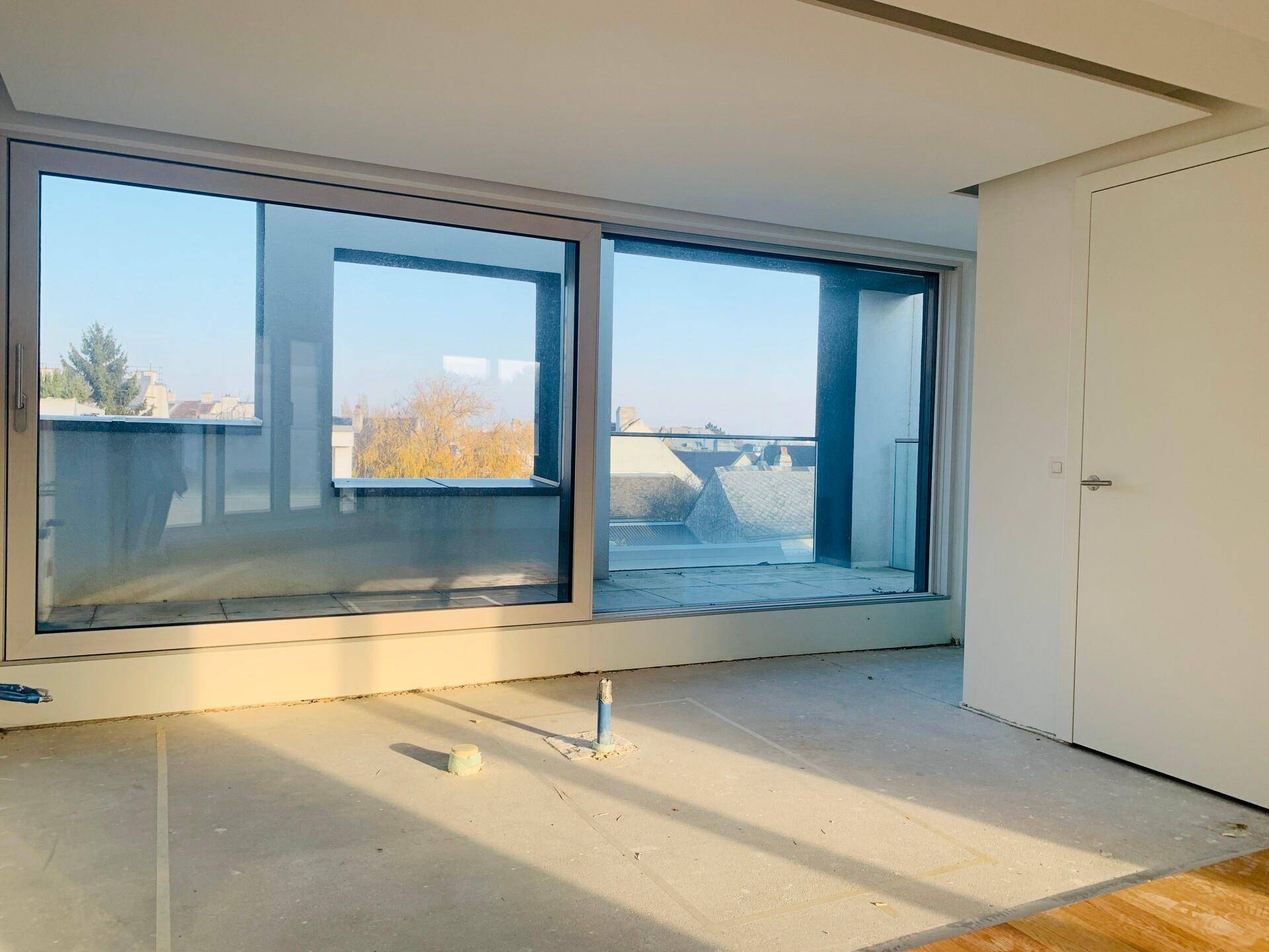 Heller Raum mit großen Schiebetüren und Blick nach draußen, noch im Rohbauzustand.
