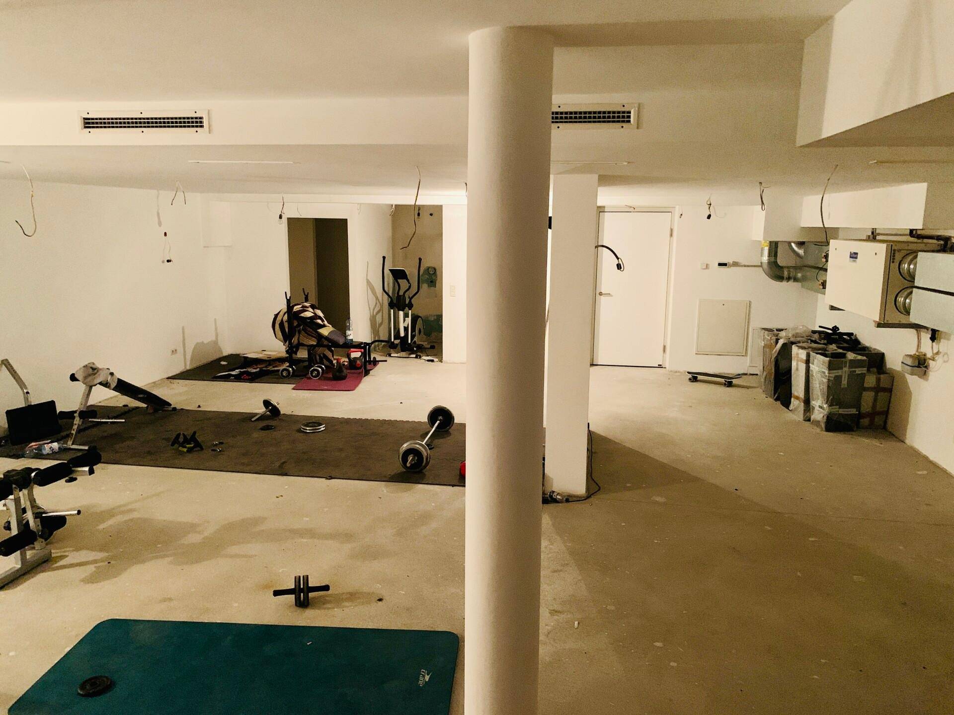 Großer Kellerraum, der als Fitnessbereich genutzt wird, mit Trainingsgeräten und Säulen.