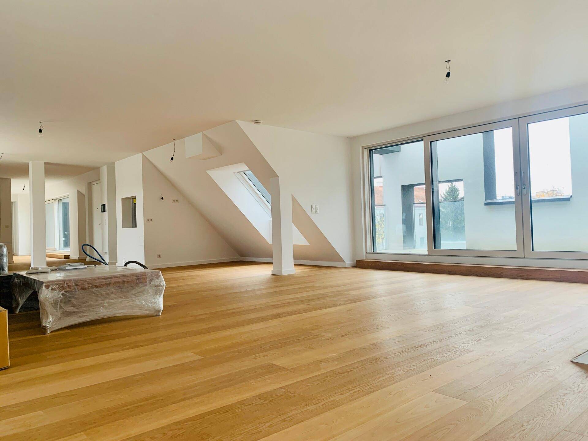Heller, leerer Raum mit Holzboden, großen Fenstern und Dachschrägen, bereit zum Einzug.