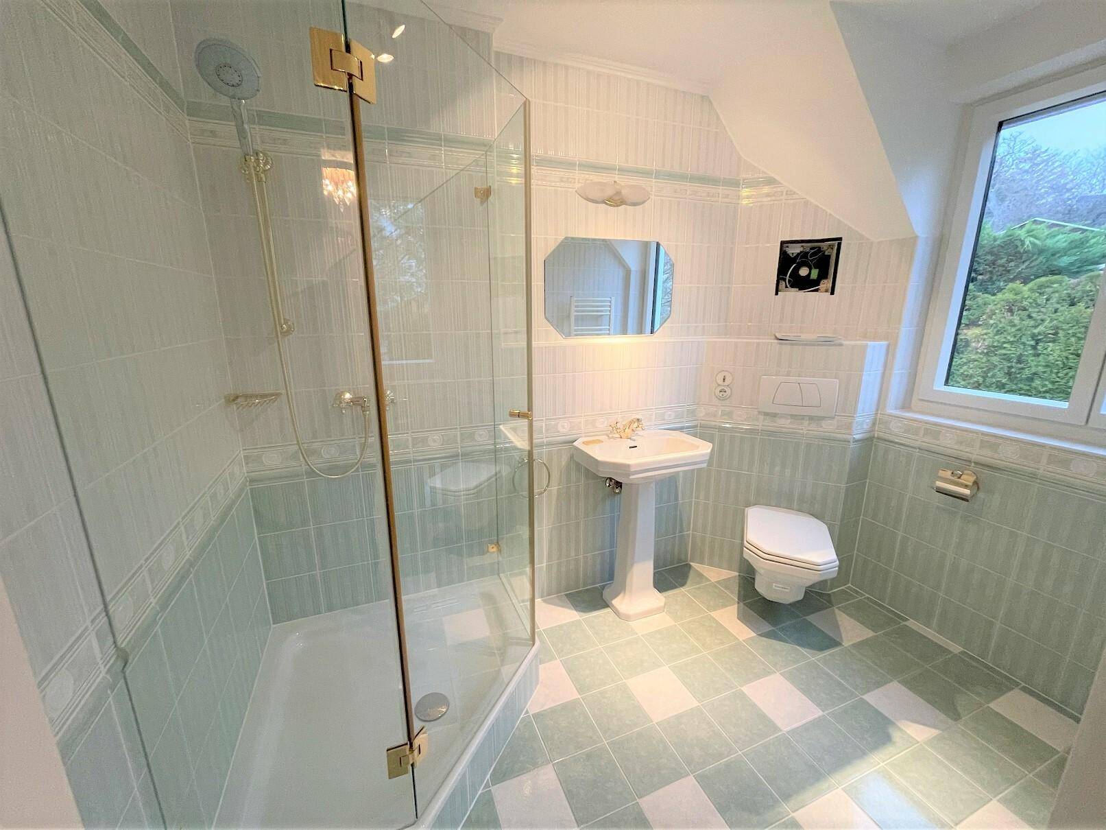 Badezimmer mit hellblauen Fliesen, Duschkabine und Fenster für Tageslicht.