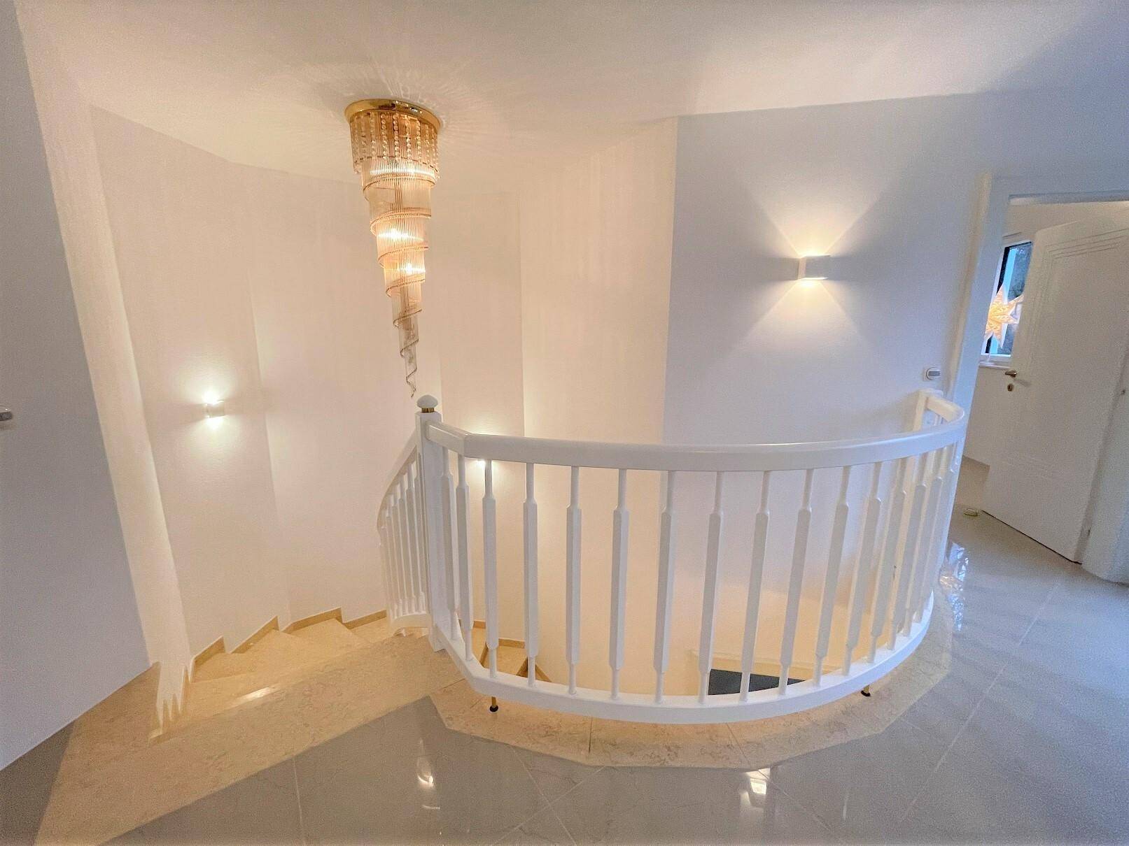 Elegantes Treppenhaus mit geschwungener Treppe und dekorativer Hängeleuchte.