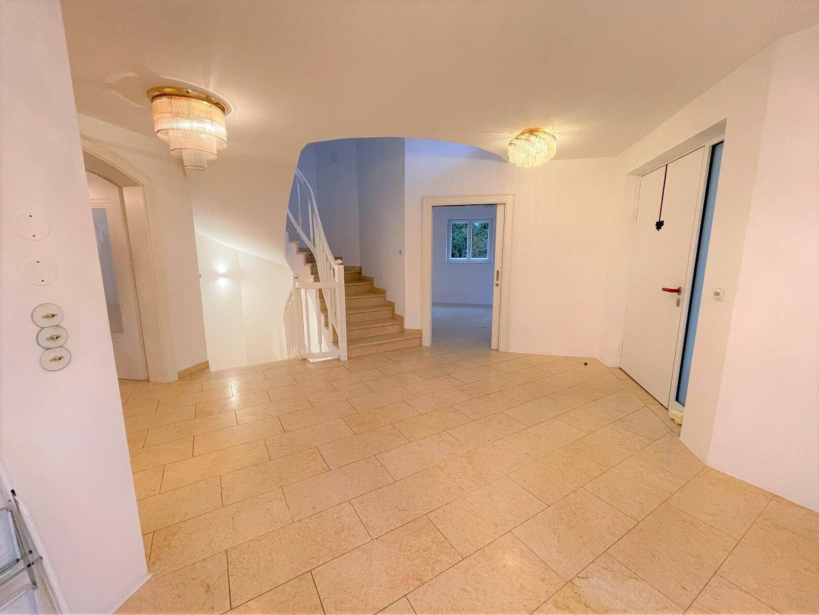 Geräumiger Flur mit heller Fliesenboden, eleganter Treppe und Zugang zu weiteren Räumen.