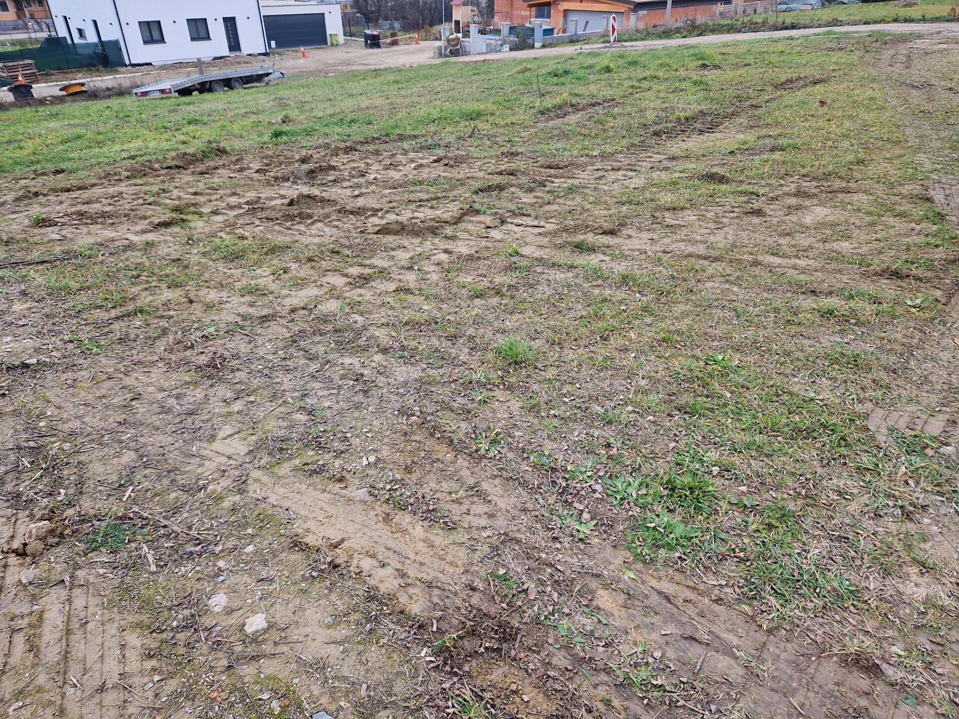 Unbebautes Grundstück mit Gras und Schlamm, gekennzeichnet durch Reifenspuren und Baustellenreste.