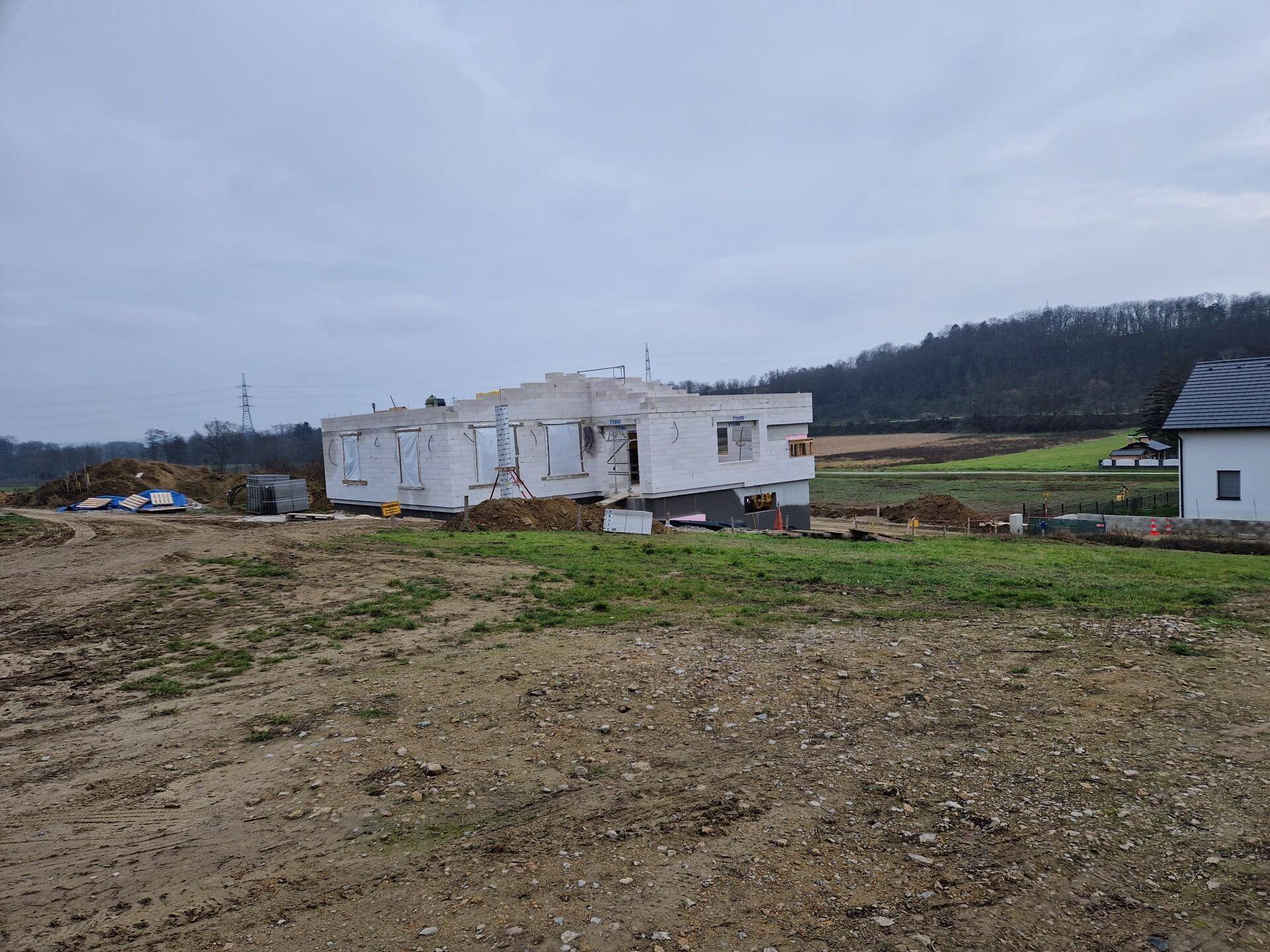 Ein im Bau befindliches Haus auf einem leicht abfallenden Grundstück mit ländlicher Kulisse.
