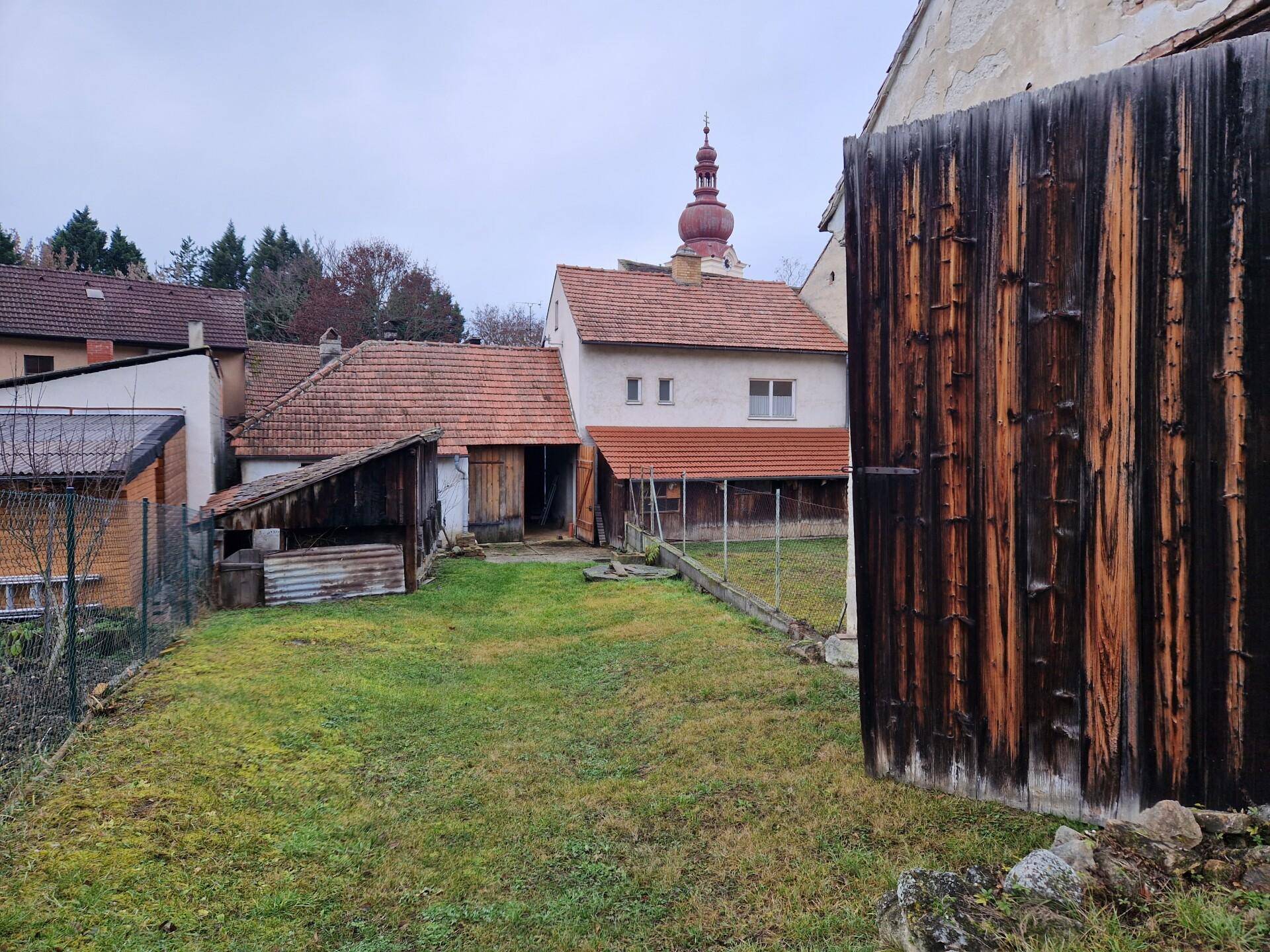 Hinterhof mit Rasenfläche, altem Holzschuppen und Blick auf die Rückseite des Hauses sowie einen Kirchturm.