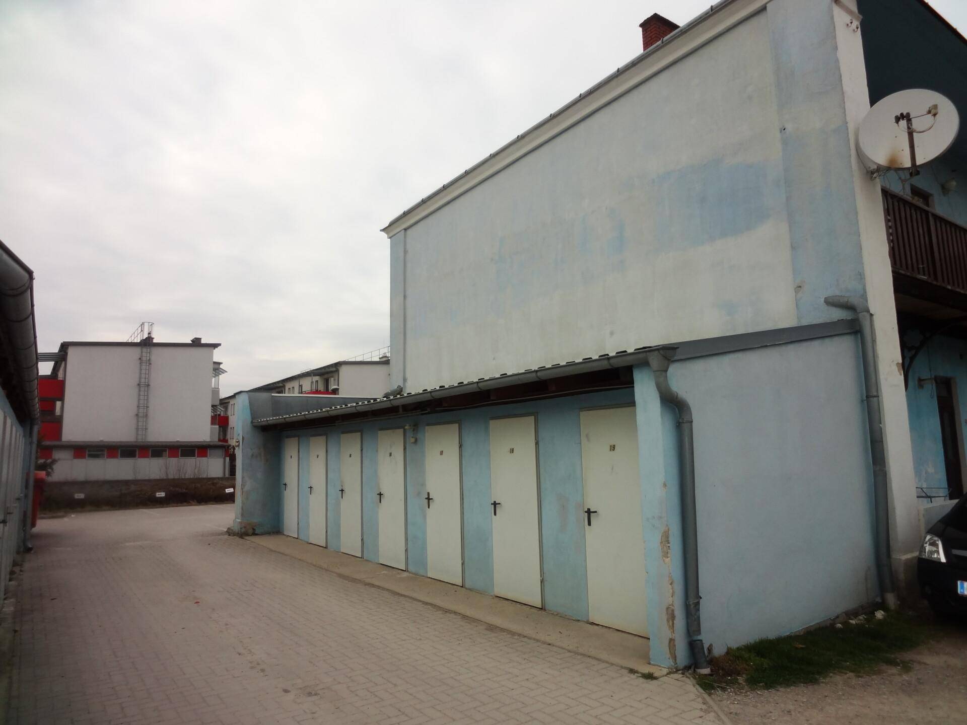 Reihe von Garagen mit weißen Toren neben einem blauen Gebäude.