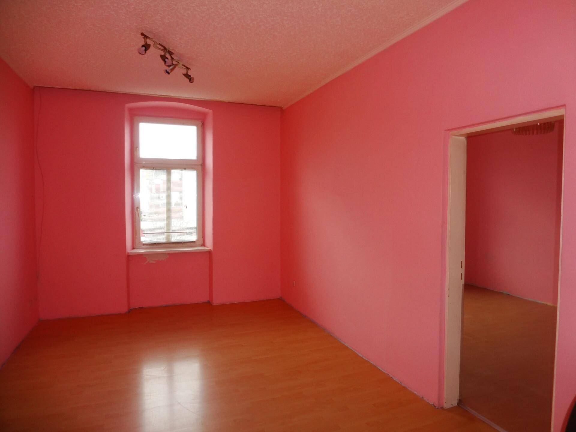 Leeres Zimmer mit leuchtend rosa Wänden und einem Fenster, bereit zur Einrichtung.