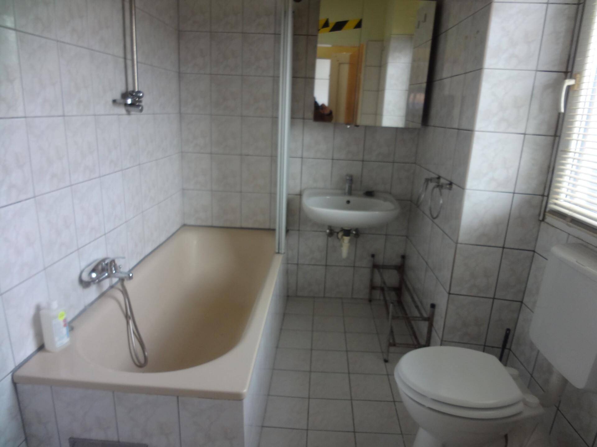 Badezimmer mit weißen Fliesen, beiger Badewanne und Toilette.