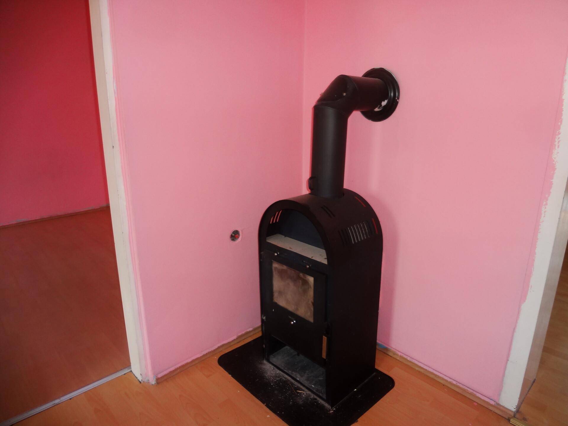 Moderner Holzofen in einer Ecke eines Zimmers mit rosa Wänden.